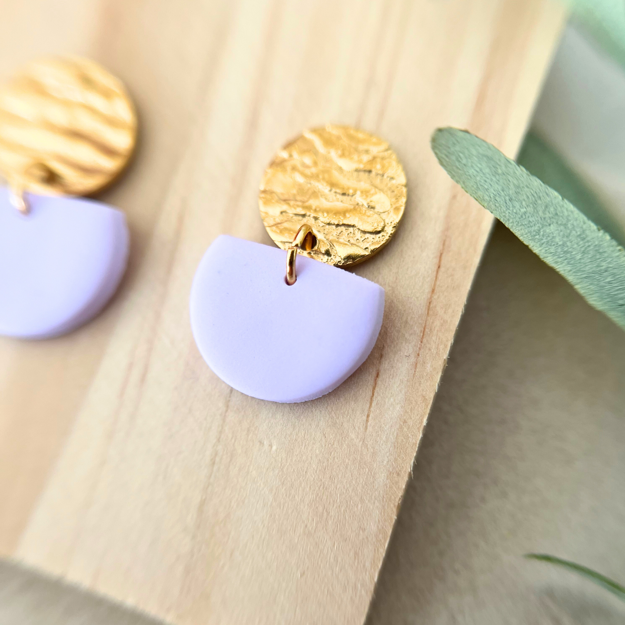 Detailaufnahme eines goldfarbenen Ohrrings ALMERIA mit eleganter Halbkreis-Form und sanften Pastelltönen aus Polymer Clay, abgebildet auf Holz