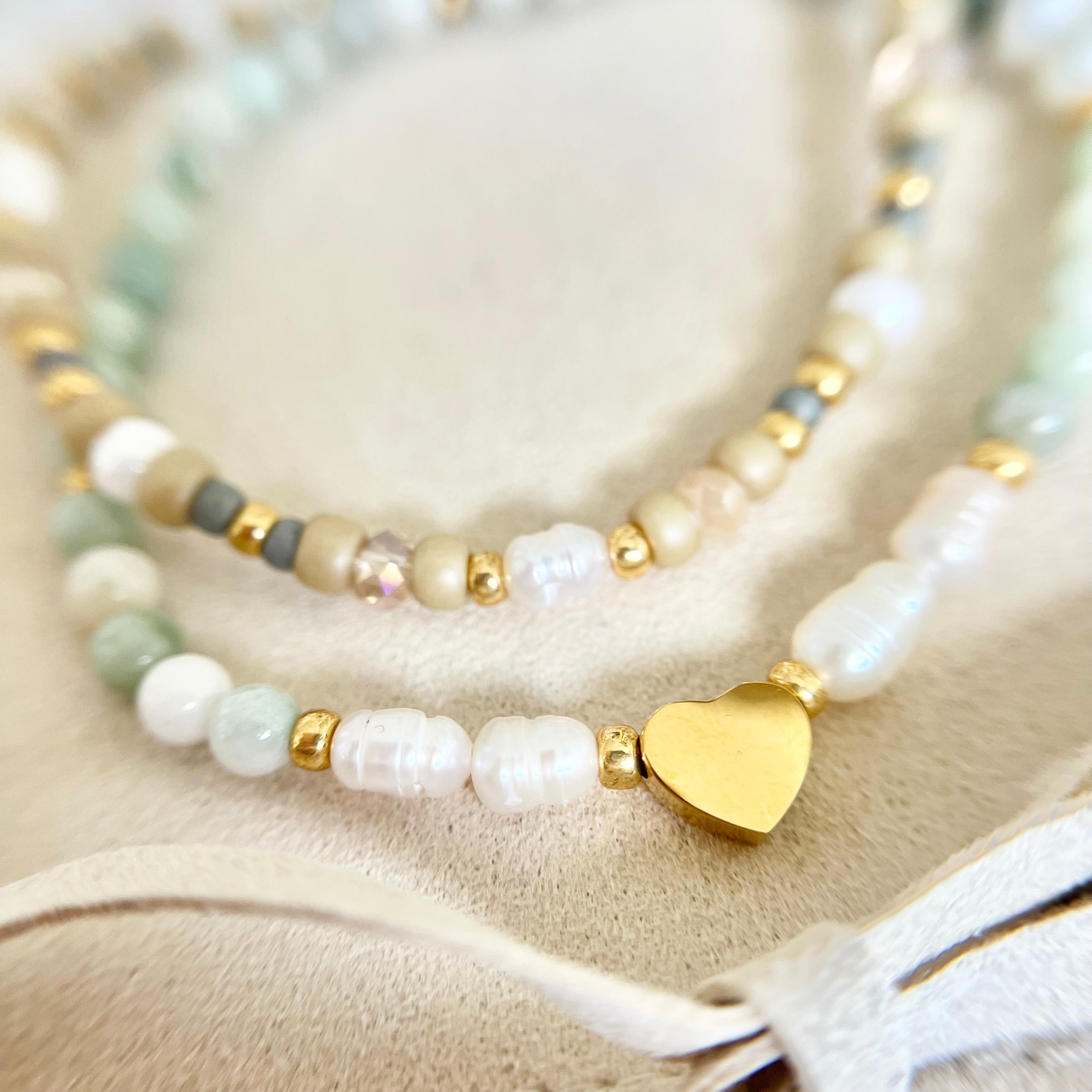 Nahaufnahme der goldenen Herzperle zwischen weißen Süßwasser- und grünen Steinperlen – ein zartes Symbol der Liebe und Freundschaft.