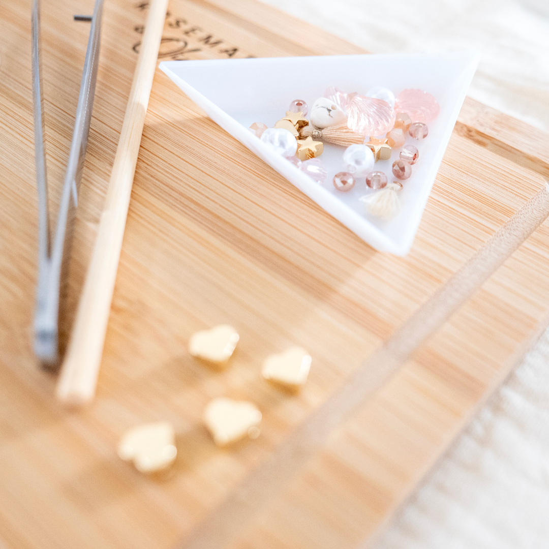 Detailaufnahme im Schmuck Workshop Wuppertal: weiße Schale mit roséfarbenen Perlen, goldenen Herzanhängern, Quaste und Werkzeug auf Holzbrett – Bastelworkshop zum Schmuck selber machen und individuelle Schmuckstücke gestalten