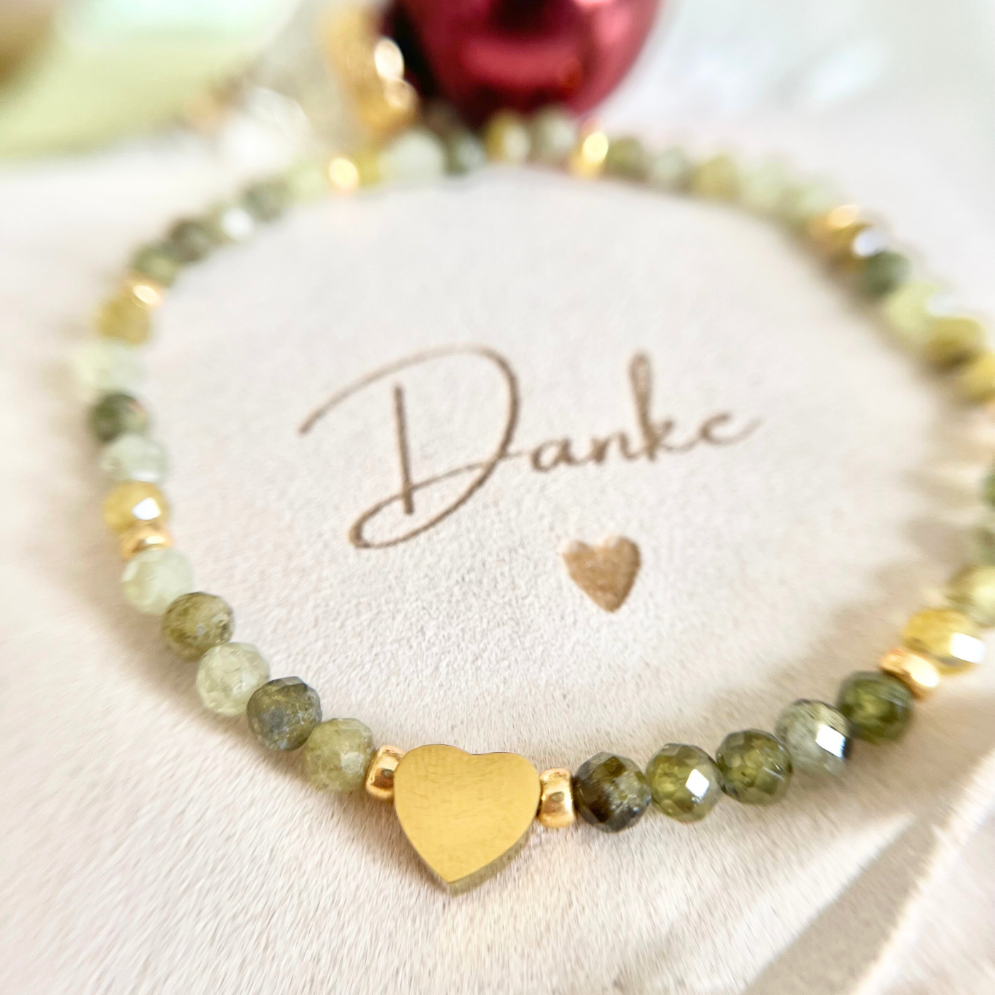 Nahaufnahme eines eleganten Armbands aus grünen Natursteinperlen mit goldfarbenen Zwischenelementen und Herz-Perle aus Edelstahl. Präsentiert auf einem beigen Schmuckbeutel mit der Aufschrift „Danke“ – stilvolles Geschenk für Weihnachten, Mama oder Trauzeugin.