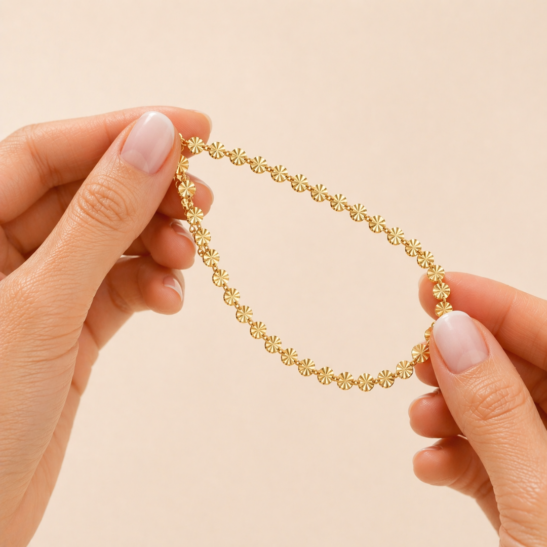 Goldenes Edelstahl Armband mit feinen Sonnen-Details wird zwischen zwei Fingern mit Babyboomer Maniküre gehalten, filigraner Damenschmuck, wasserfest und elegant