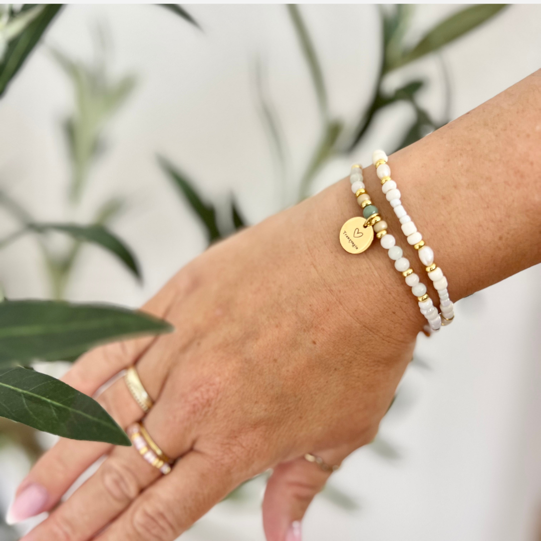 Zwei zarte Armbänder aus weißen Perlen mit goldenen Akzenten, eines mit graviertem „Trauzeugin“-Anhänger, getragen am Handgelenk – liebevolles, handgemachtes Schmuck-Set als Geschenk zur Trauzeugin-Frage oder Hochzeit.