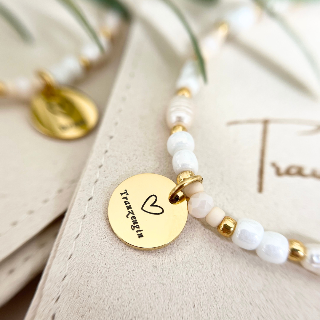 Nahaufnahme eines eleganten Armbands aus echten Süßwasserperlen und goldfarbenem Edelstahlanhänger mit Herz und Schriftzug „Trauzeugin“ – stilvolles Freundschaftsarmband für Hochzeit oder Verlobung