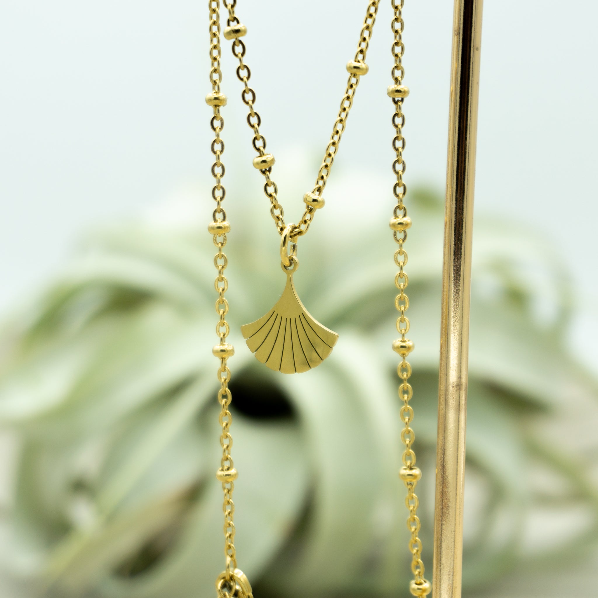 Goldene Edelstahlkette DEIA hängt herab, mit Fokus auf den Ginkgo-Blatt Anhänger, der dem Schmuckstück eine bedeutungsvolle Note verleiht.
