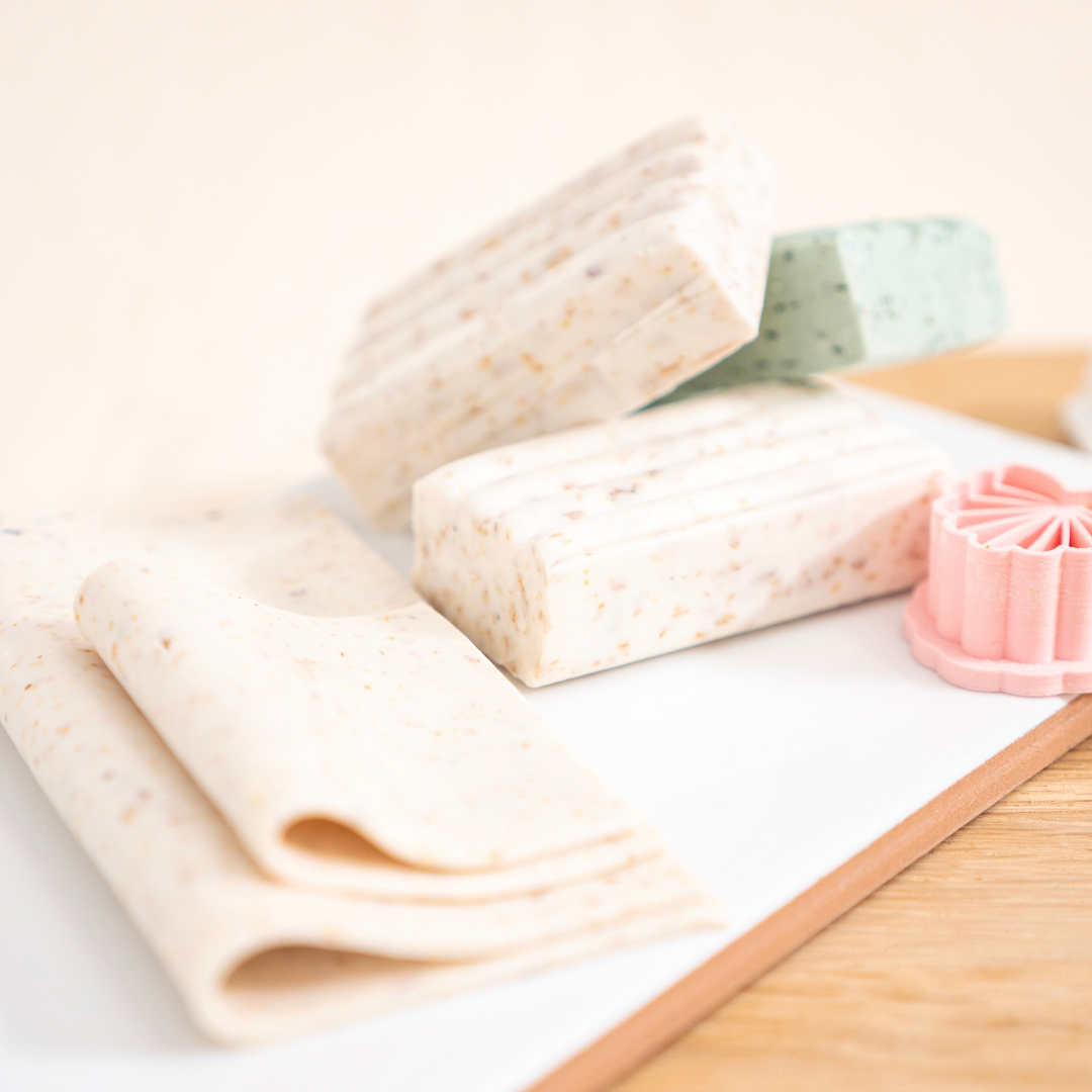 Mehrere Blöcke und ausgerollte Platten aus heller Polymer Clay Modelliermasse mit Naturfasern in Beige, Grün und Rosa – vorbereitet für den Kreativ Workshop in Wuppertal, daneben ein pinker Ausstecher zur Schmuckherstellung