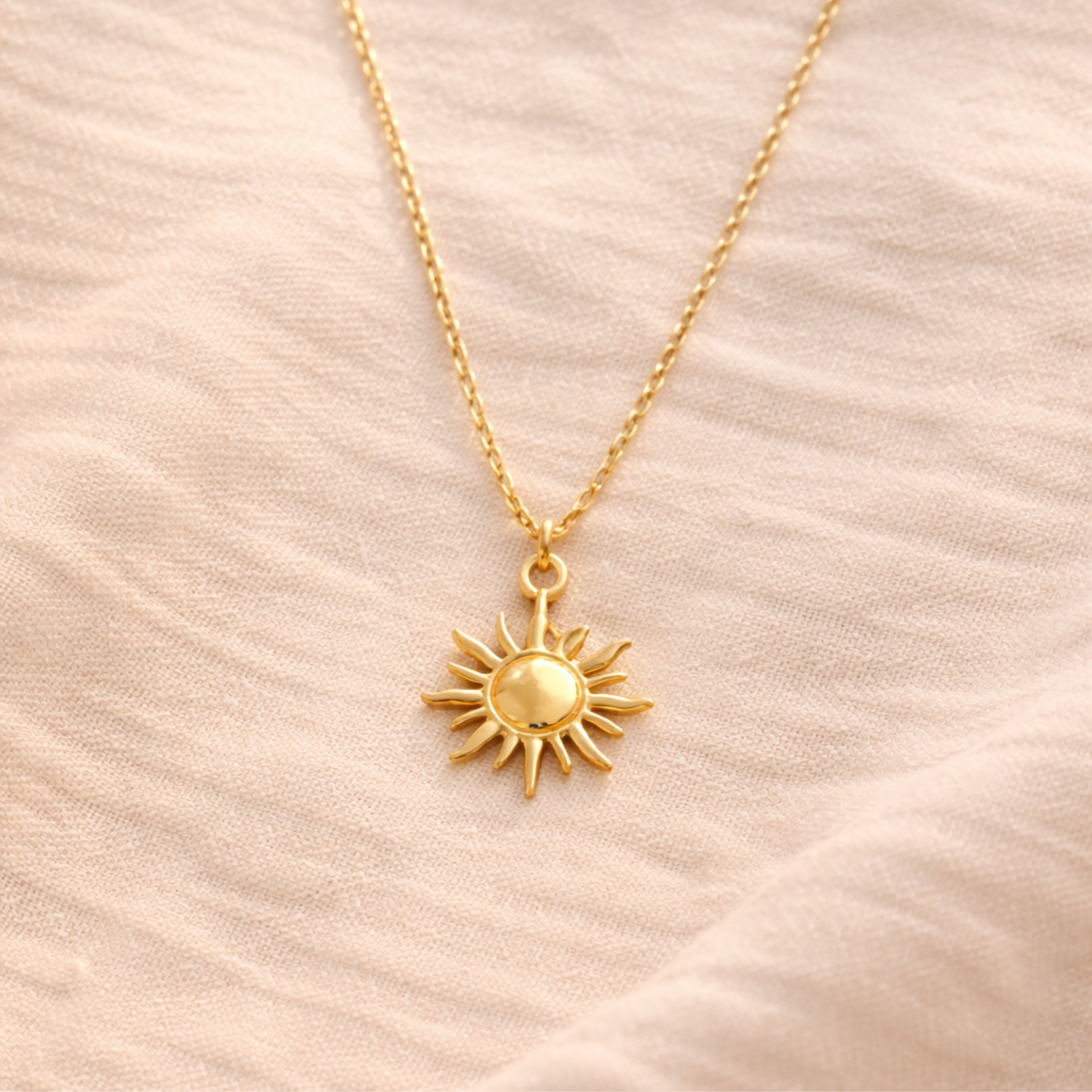 Goldene Sonnenkette aus Edelstahl auf beigem Leinenstoff, minimalistische Produktaufnahme mit weichem Licht und feiner Kettenstruktur