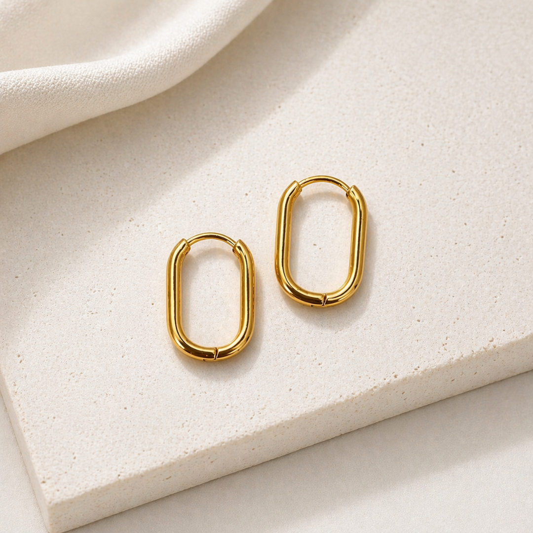 Goldene Huggie Hoops Creolen aus Edelstahl auf hellem Stein, ovale kleine Ohrringe, wasserfester minimalistischer Schmuck