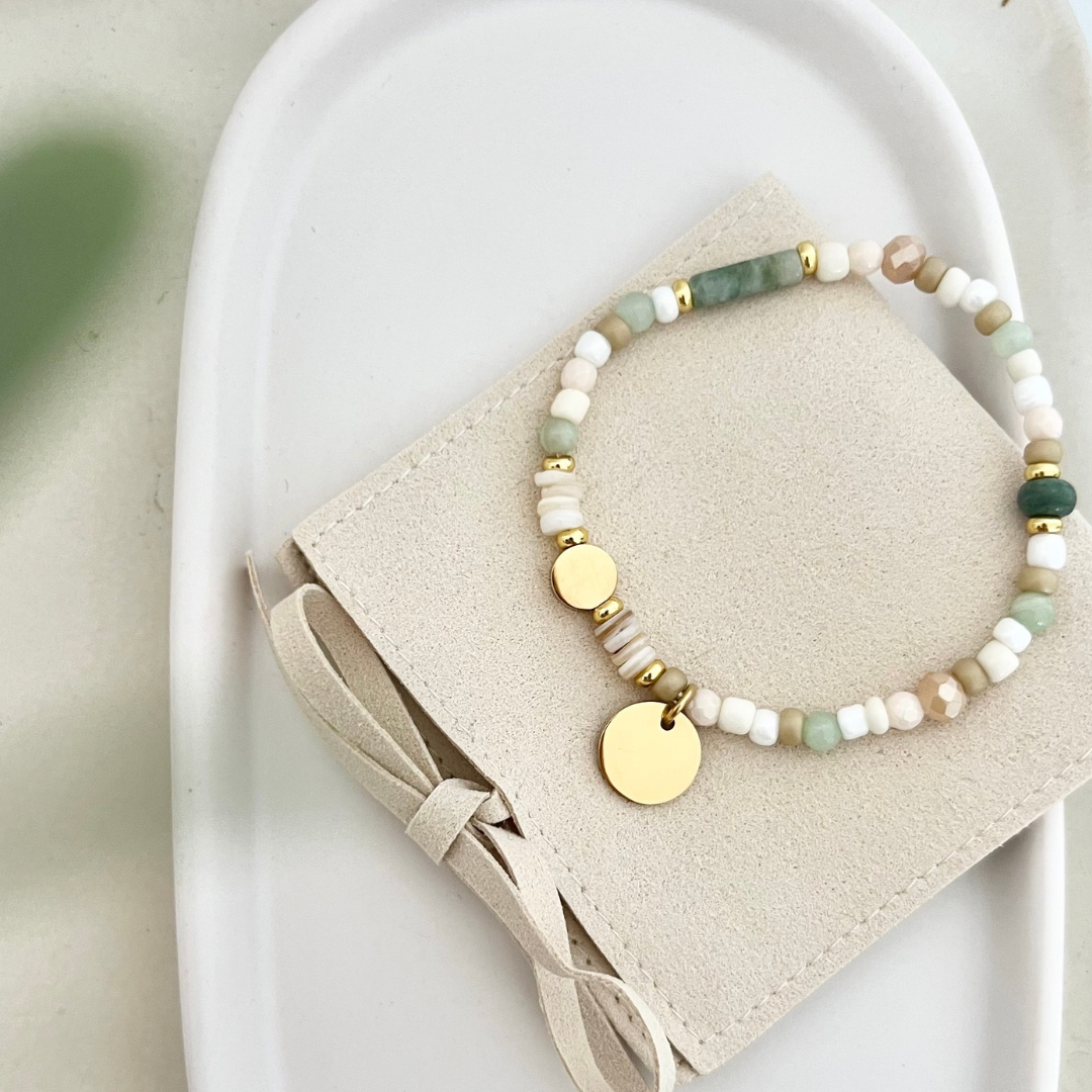 Gesamtansicht des Armbands liegend auf einer Tasche – filigranes Armband mit Aventurin- und Muschelperlen, edel in Weiß und Beige