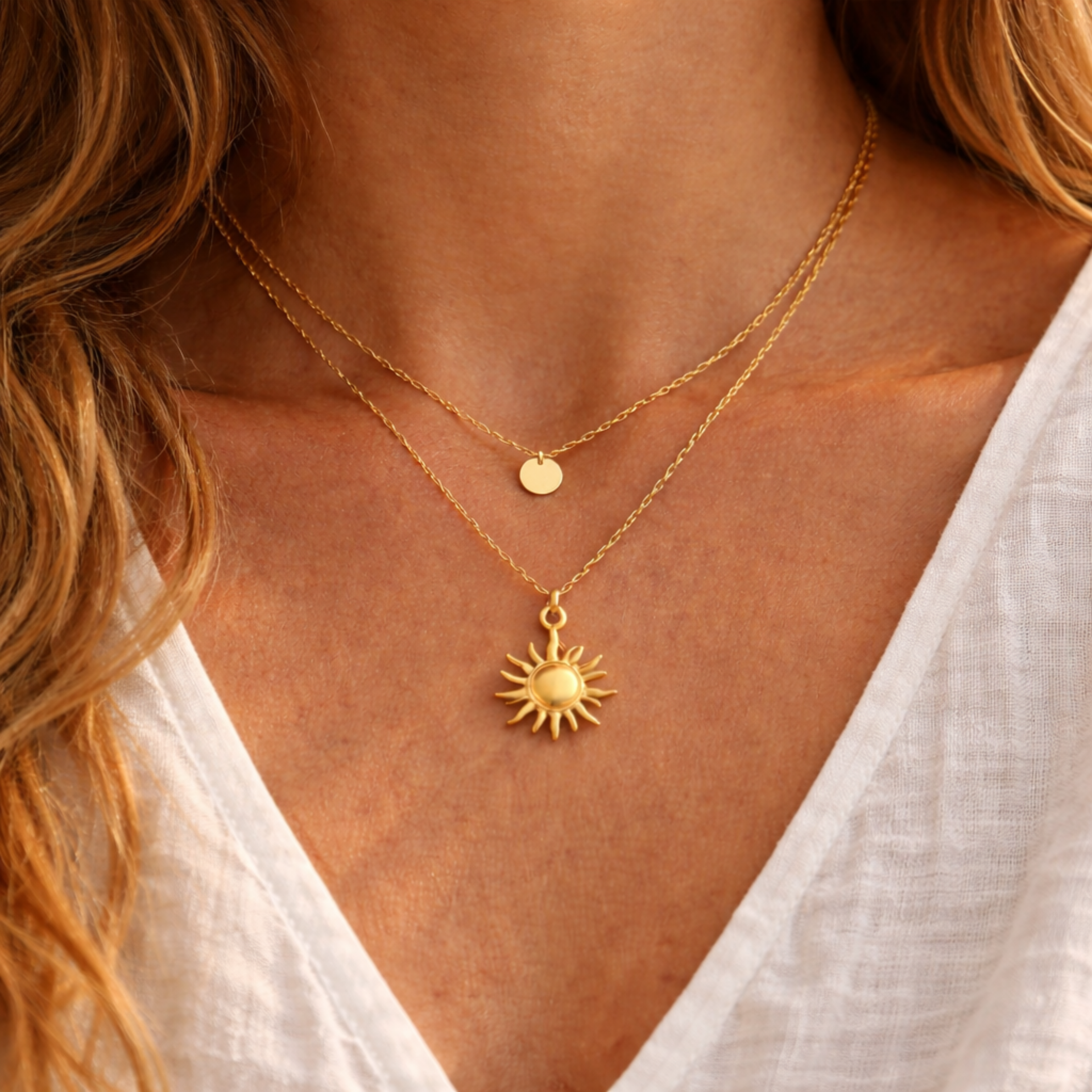 Goldene Sonnenkette aus Edelstahl im Layering Look kombiniert mit feiner goldener Kette mit Plättchen, getragen auf gebräunter Haut mit weißer Bluse