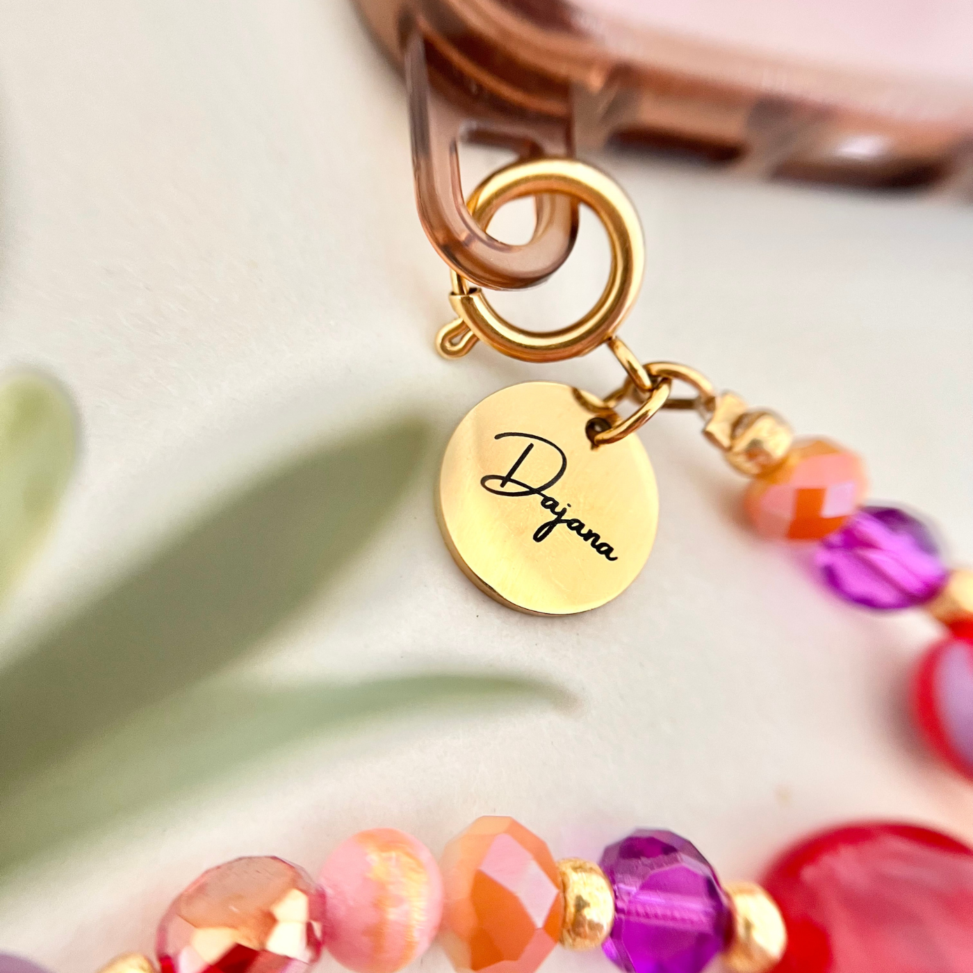 Detailaufnahme des gravierten Edelstahl-Anhängers mit Namen an einer bunten Handykette – personalisiertes Handyband mit Perlen für Handyhüllen mit Ösen.
