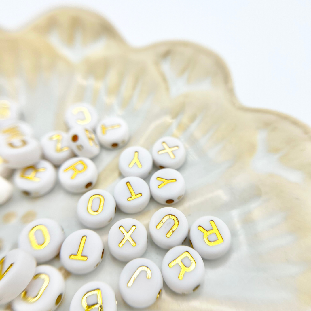 Nahaufnahme von Buchstabenperlen mit schwarzer und goldener Schrift, ideal für Freundschaftsarmbänder und Geschenke