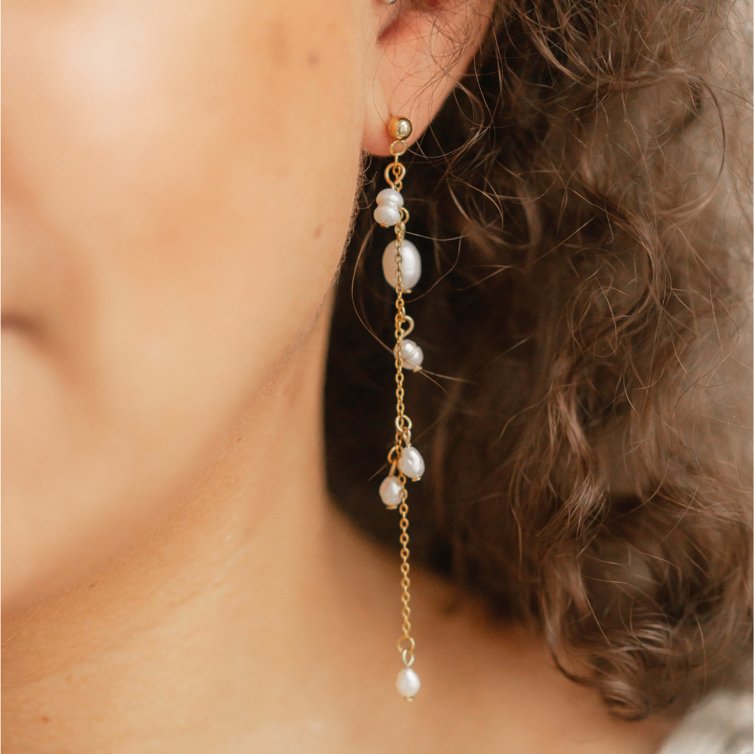 Nahaufnahme eines Ohrrings EVA, getragen von einem Model, das die Süßwasserperlen und das elegante Design mit goldfarbenen Kettengliedern zur Geltung bringt.