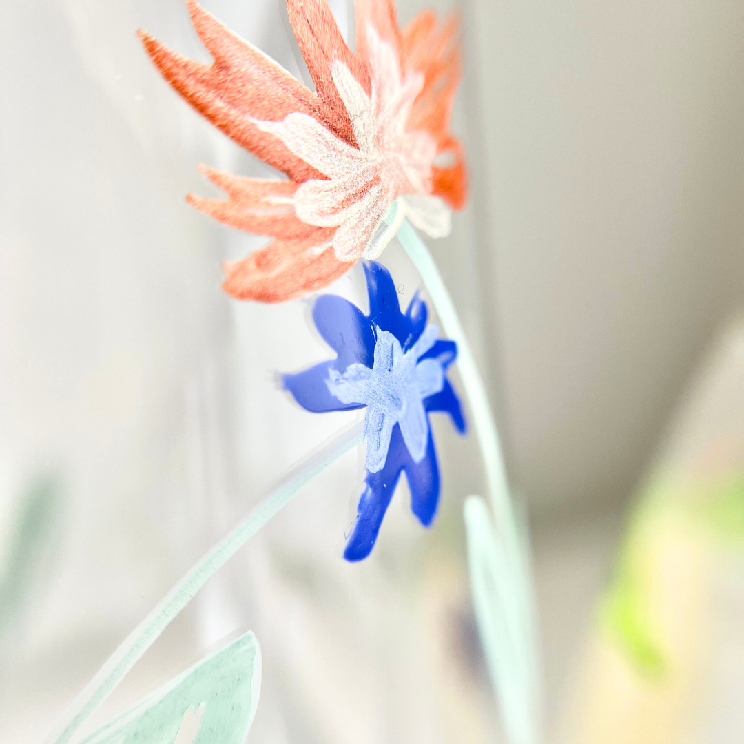 Makro Aufnahme von handgemalter Glasmalerei mit zwei Blumen in Metallic Orange und Blau auf einem Weinglas – filigrane boho Blütenmotive aus dem Glass Painting Workshop in Wuppertal, ideal zum Gläser bemalen mit Farbe und Pinsel