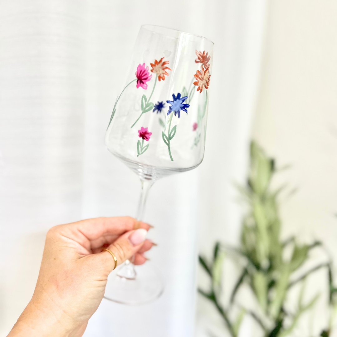 Hand bemaltes Weinglas mit zarten Wildblumen in Rosa, Blau, Orange und Grün – florales Design mit Stängeln und Blüten aus dem Glass Painting Workshop in Wuppertal, ideal für individuelle Glasgestaltung und kreative Auszeiten