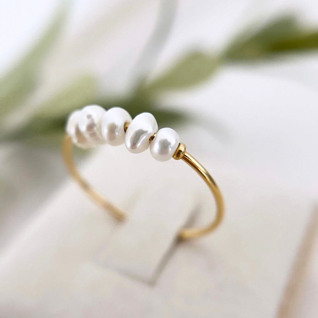 Goldener Ring mit zarten Süßwasserperlen, minimalistisch und elegant, auf einem hellen Hintergrund präsentiert – perfektes Schmuckstück für zeitlose Eleganz