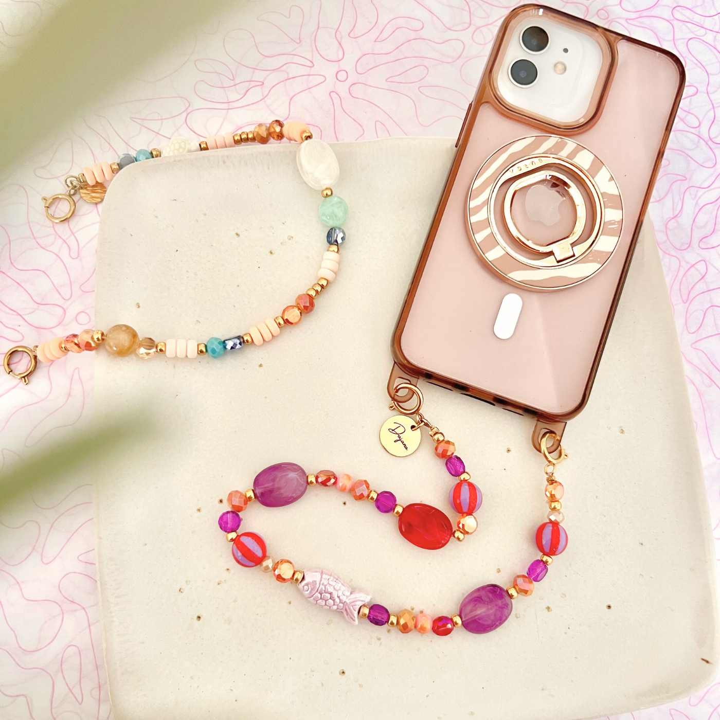 Gesamtansicht einer personalisierten Handykette mit bunten Perlen, Keramik-Fisch und graviertem Namensanhänger neben einem Smartphone – dekoratives Handyband für Handyhüllen mit Ösen.