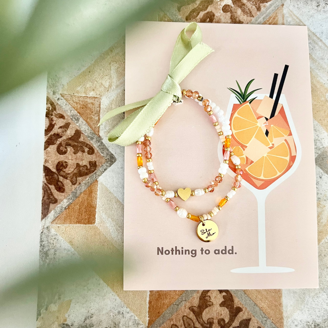 Zwei Perlenarmbänder auf illustrierten Cocktail-Postkarte mit Orangenmotiv und grüner Schleife. Geschenkfertiges Sommerduo mit warmen Farbtönen und Herz-Detail – ideal für Freundinnen. Typisches Aperol Armband.