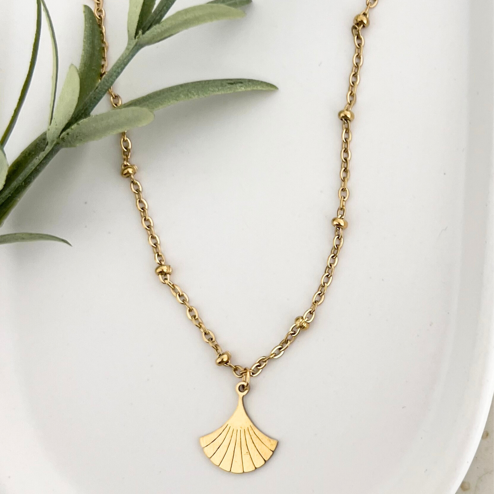 Goldene Edelstahlkette DEIA auf einem weißen Tablet, der Ginkgo-Blatt Anhänger wird gezeigt, der das elegante Design unterstreicht.