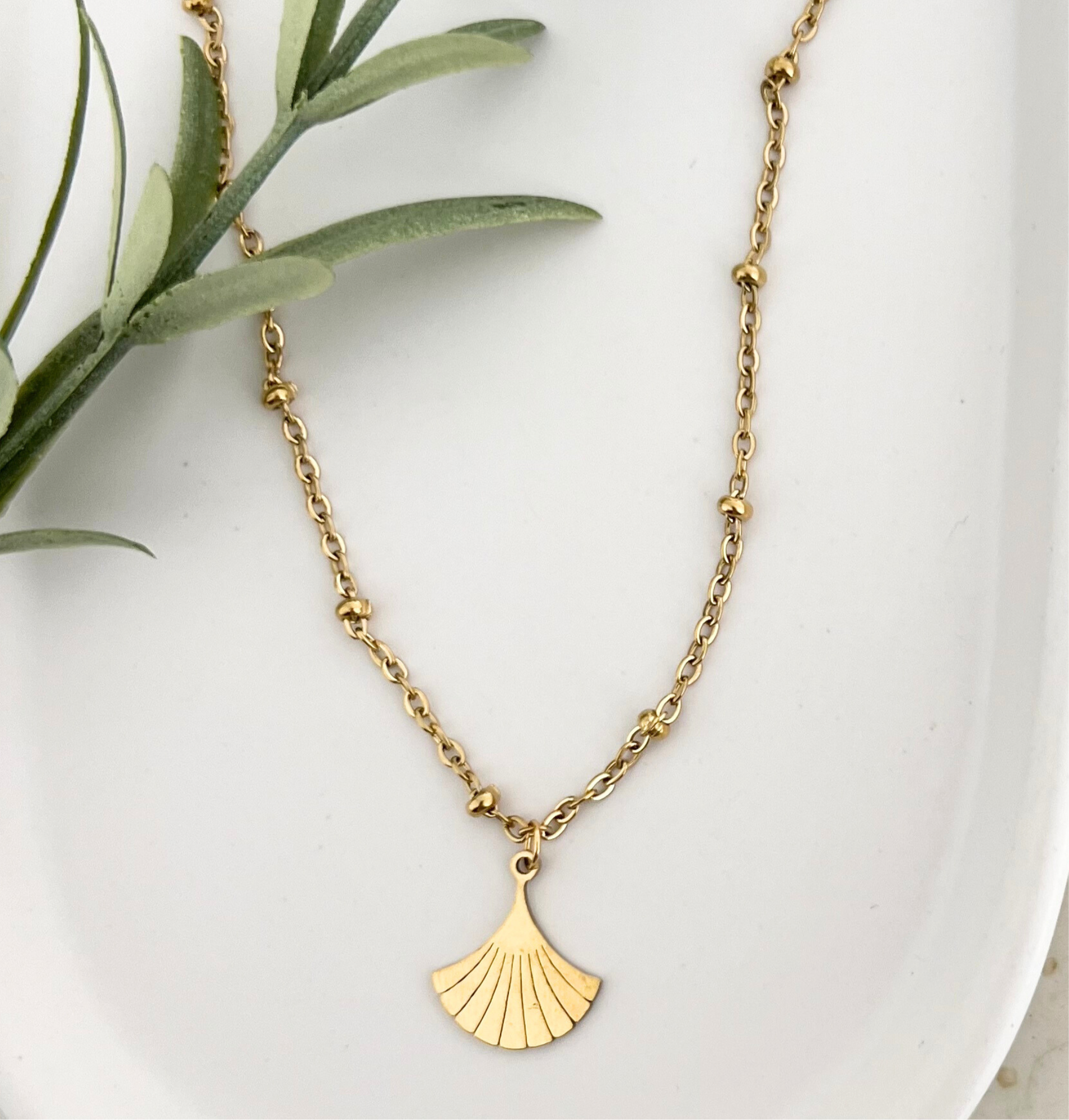 Goldene Edelstahlkette DEIA auf einem weißen Tablet, der Ginkgo-Blatt Anhänger wird gezeigt, der das elegante Design unterstreicht.