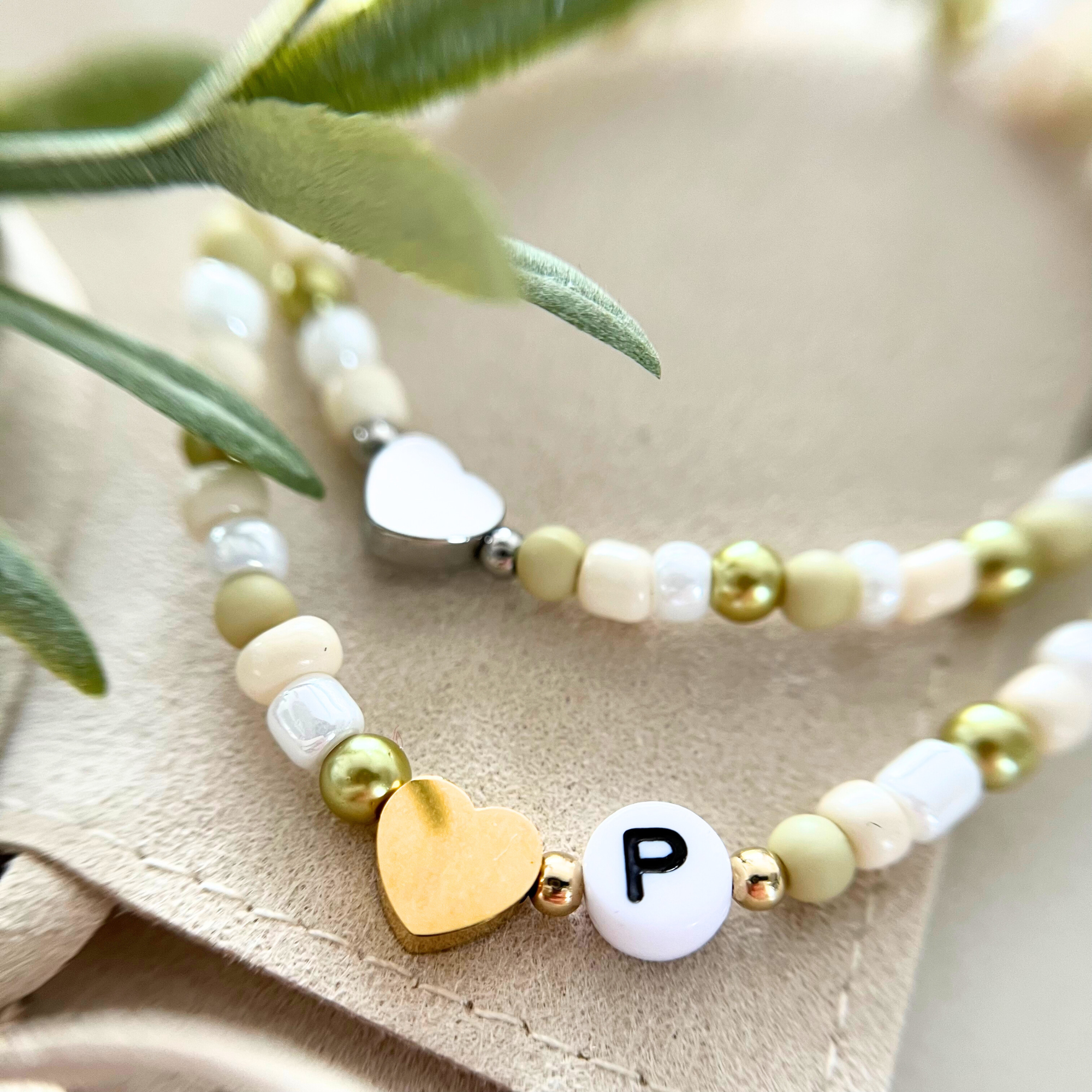 Zwei handgemachte Armbänder aus dem DIY Kit VERDE – eines mit goldenem Herzanhänger und das andere mit einem silbernen Anhänger und Buchstaben „P“. Perfekt für Junggesellinnenabschiede, Freundschaftsarmbänder und kreative Bastelstunden.