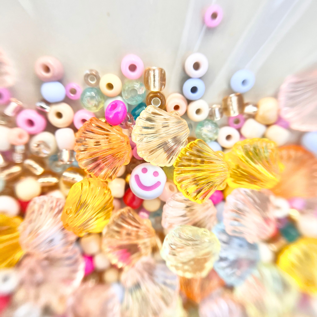 Nahaufnahme von bunten Perlen mit Smiley-Perle und transparenten Muschelperlen in Gelb, Orange und Rosa