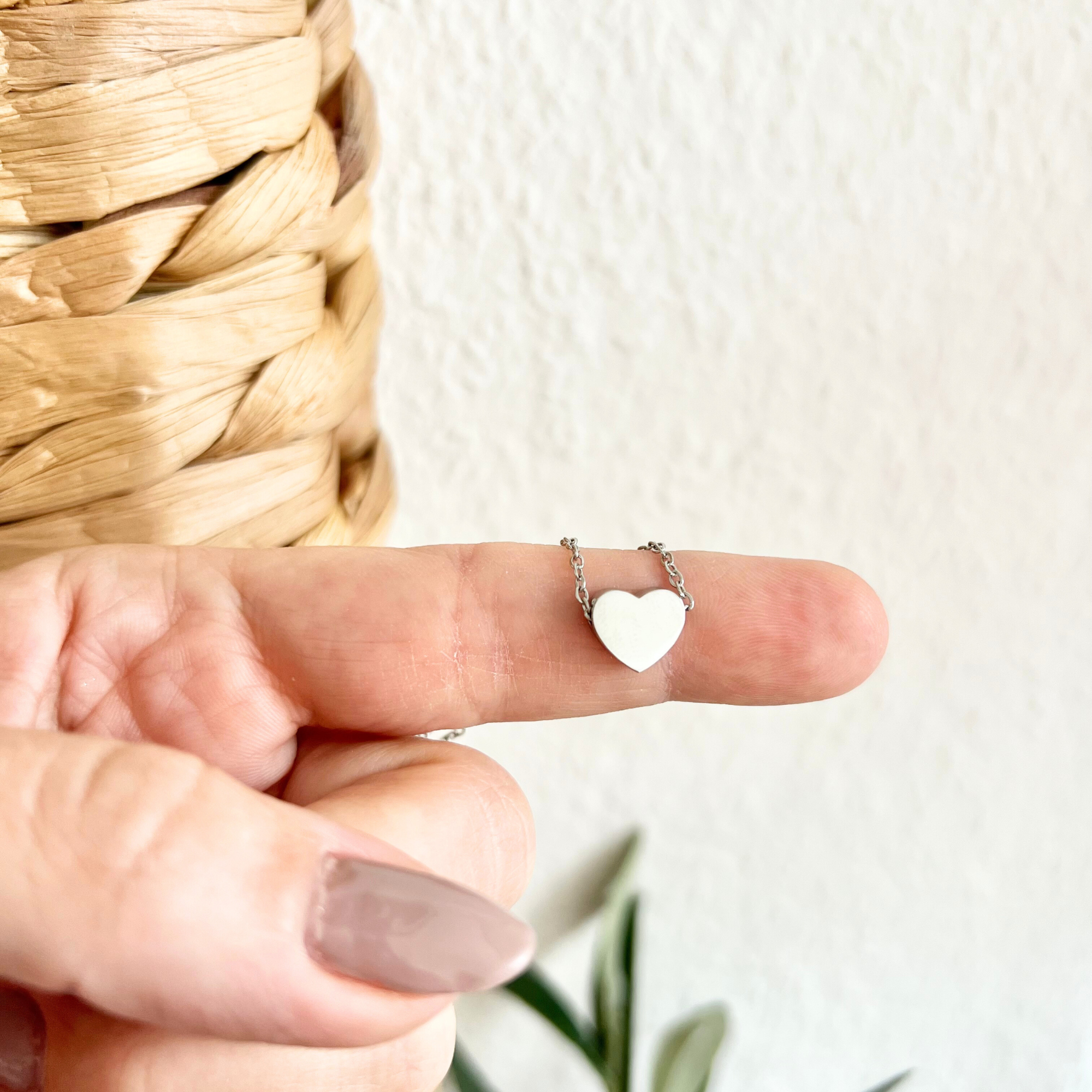 Personalisierte Herzkette aus Edelstahl mit graviertem Namen auf Herzanhänger, minimalistische Halskette in Silber auf Finger gehalten