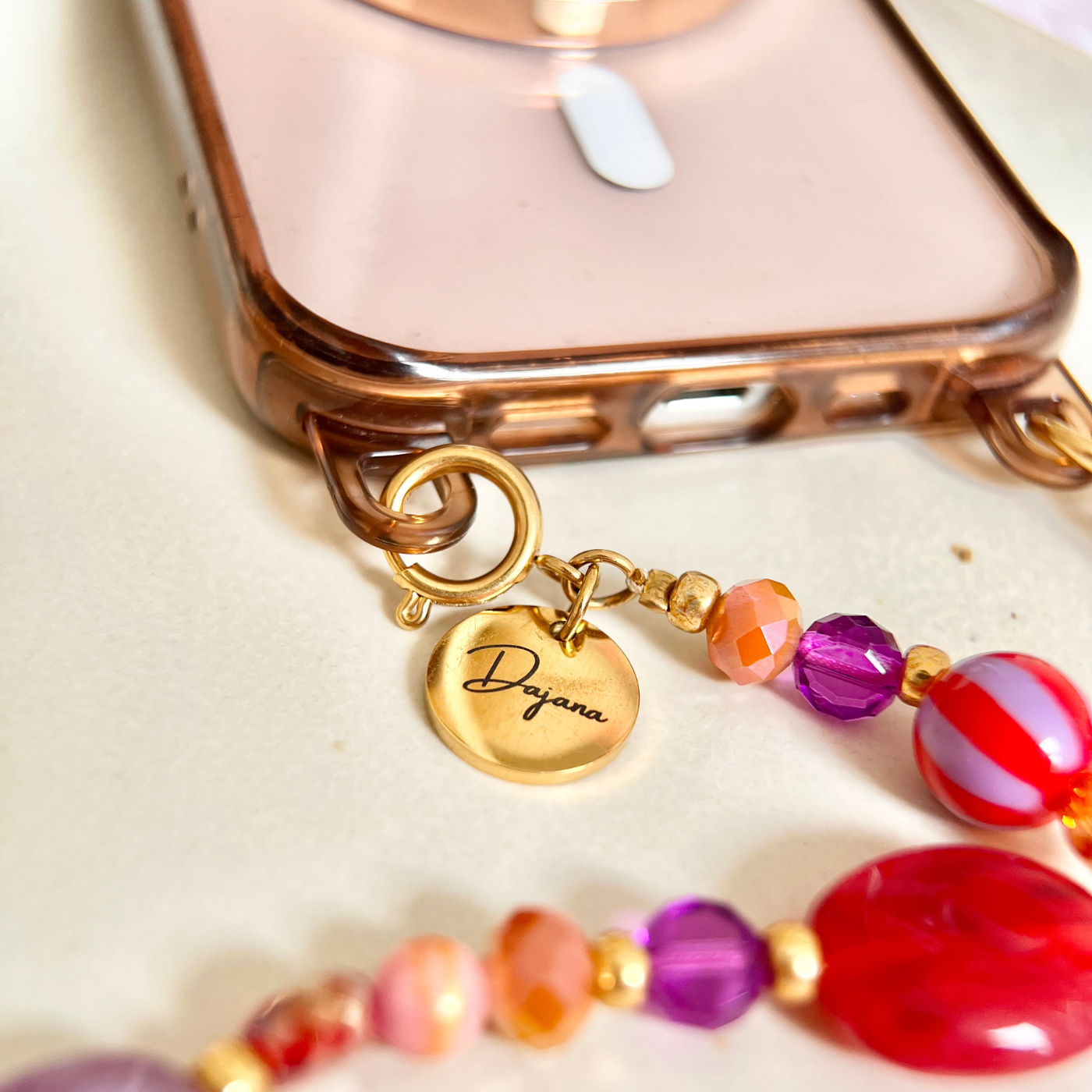 Personalisierte Handykette mit bunten Perlen und graviertem Edelstahl-Anhänger mit Namen „Dajana“, befestigt an einer Handyhülle mit Ösen – praktisches und dekoratives Handyband.