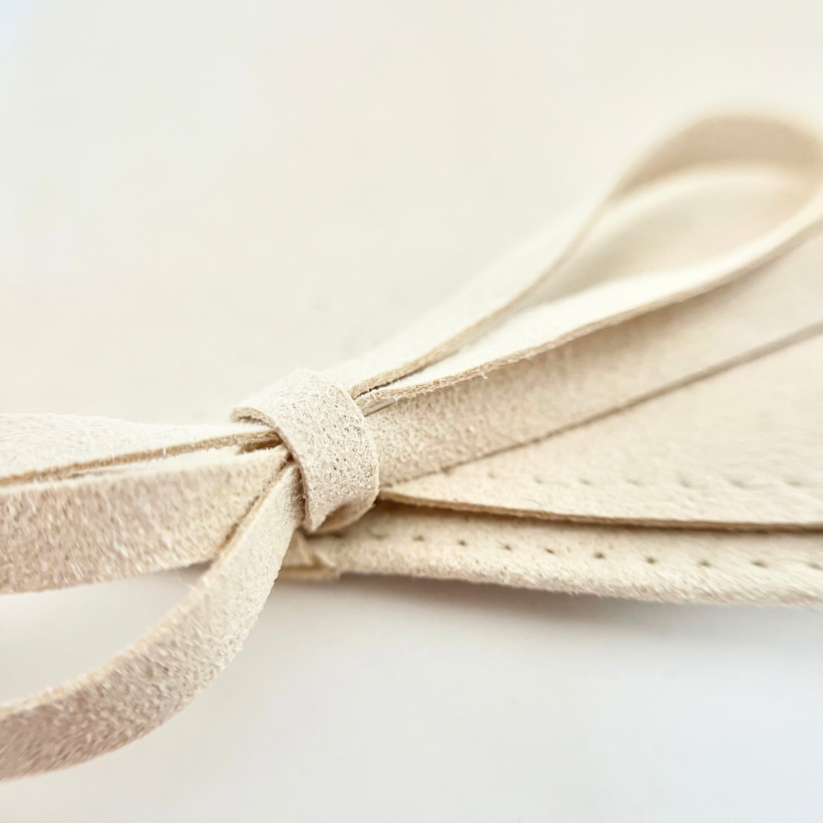 Nahaufnahme eines hellbeigen, samtweichen Schmuckbeutels mit gebundener Schleife aus Velours bzw. Mikrofaser, fotografiert auf weißem Hintergrund.