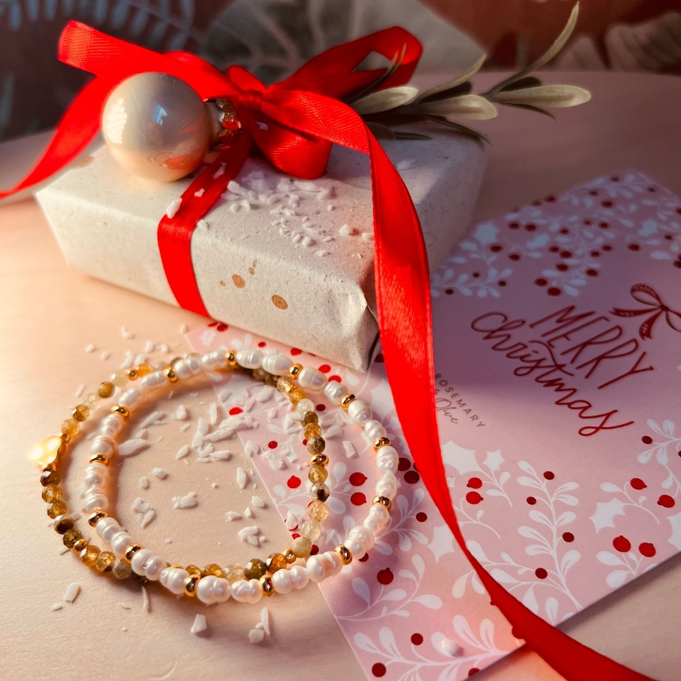 Perlenarmband mit Gravur-Anhänger „Beste Mama“ zwischen Weihnachtskugeln und festlicher Deko als liebevolles Geschenk zu Weihnachten.