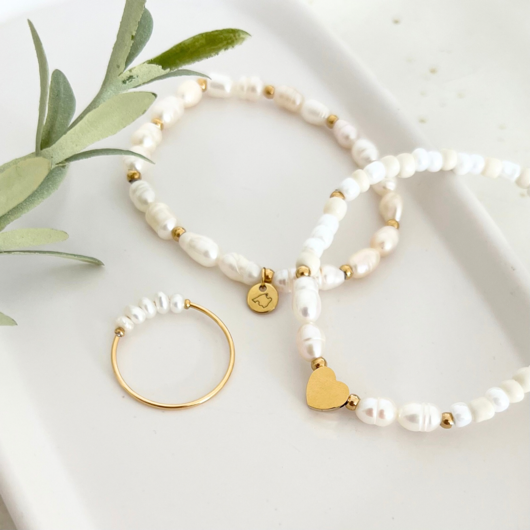 Set aus goldfarbenem Ring mit Süßwasserperlen und passenden Armbändern mit Perlen, Mallorca Anhänger, goldenen Akzenten und Herzanhänger, auf einem weißen Tablett mit grüner Dekoration – stilvoller Perlenschmuck für jeden Anlass