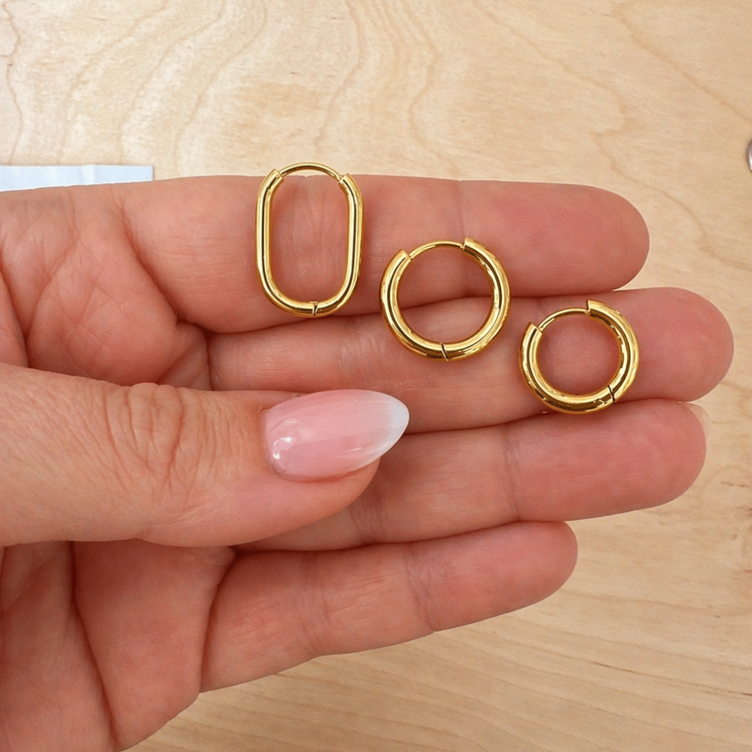 Hand hält drei goldene Edelstahl Creolen in oval und rund, Huggie Hoops Ohrringe für Mix & Match Kombination