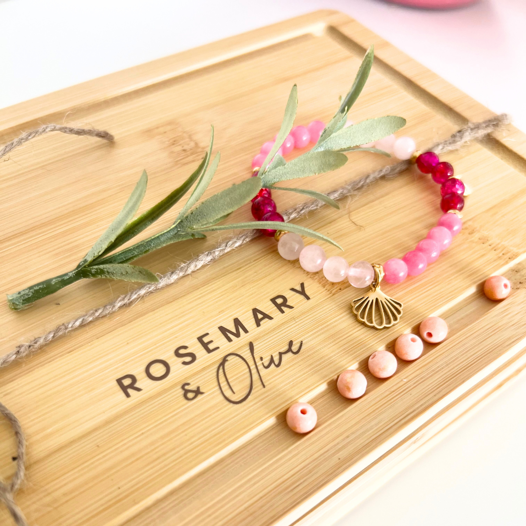 Schmuckbrett mit Logo ‚Rosemary & Olive‘ zum kreativen Anordnen von Perlen – rosa Natursteinperlen, goldener Muschelanhänger und DIY Armband als Teil des Schmuck Workshops in Wuppertal für Anfänger und Mädelsabende