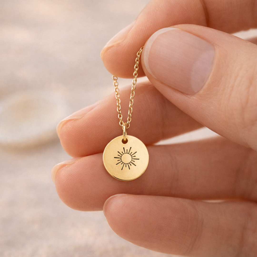 Hand hält eine feine goldene Kette mit rundem Anhänger und Sonnenmotiv, geeignet als persönliches Schmuckstück oder Geschenk mit optionaler Gravur