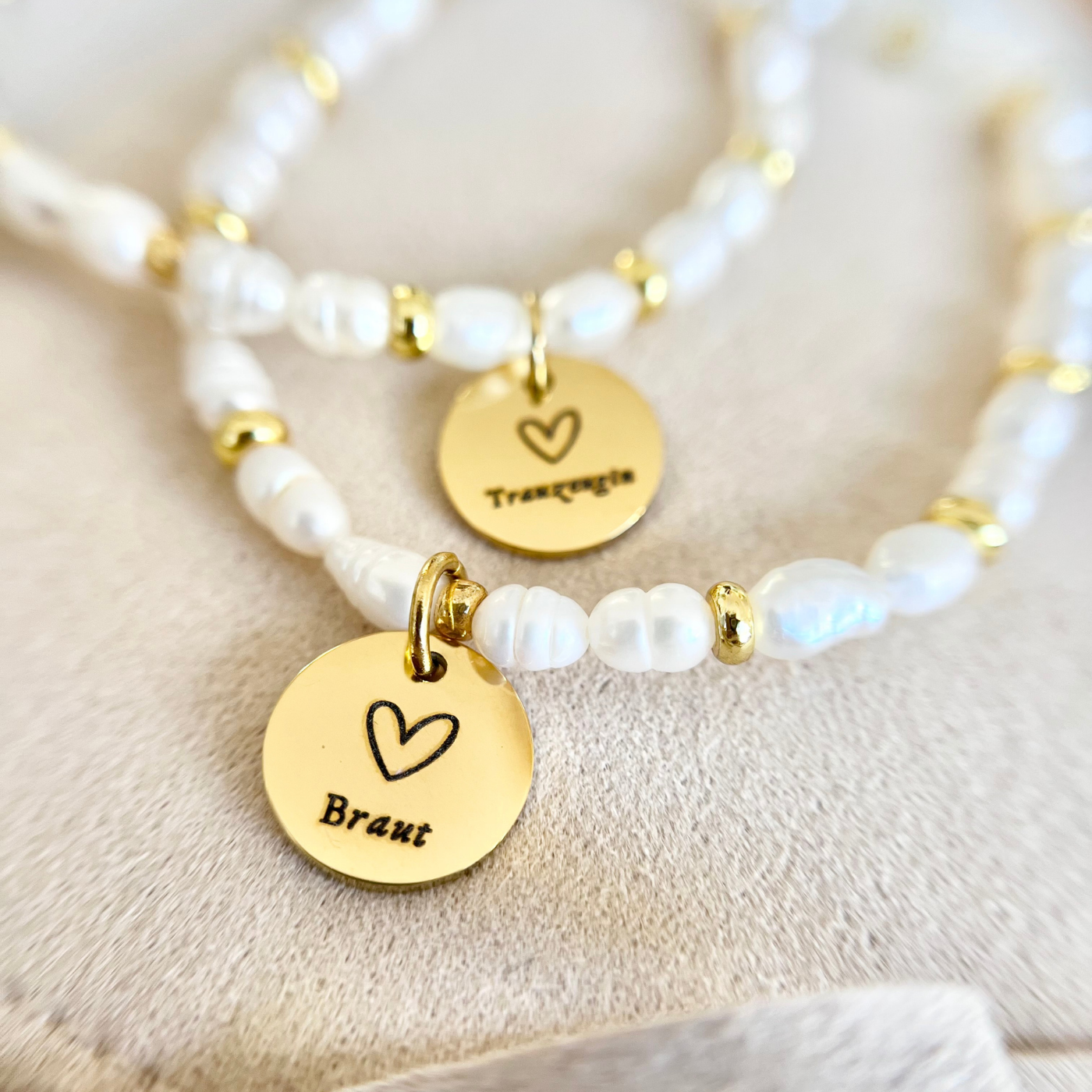 Makroaufnahme eines runden, goldfarbenen Edelstahl Anhängers mit Gravur „Braut“, befestigt an einem Süßwasserperlenarmband.