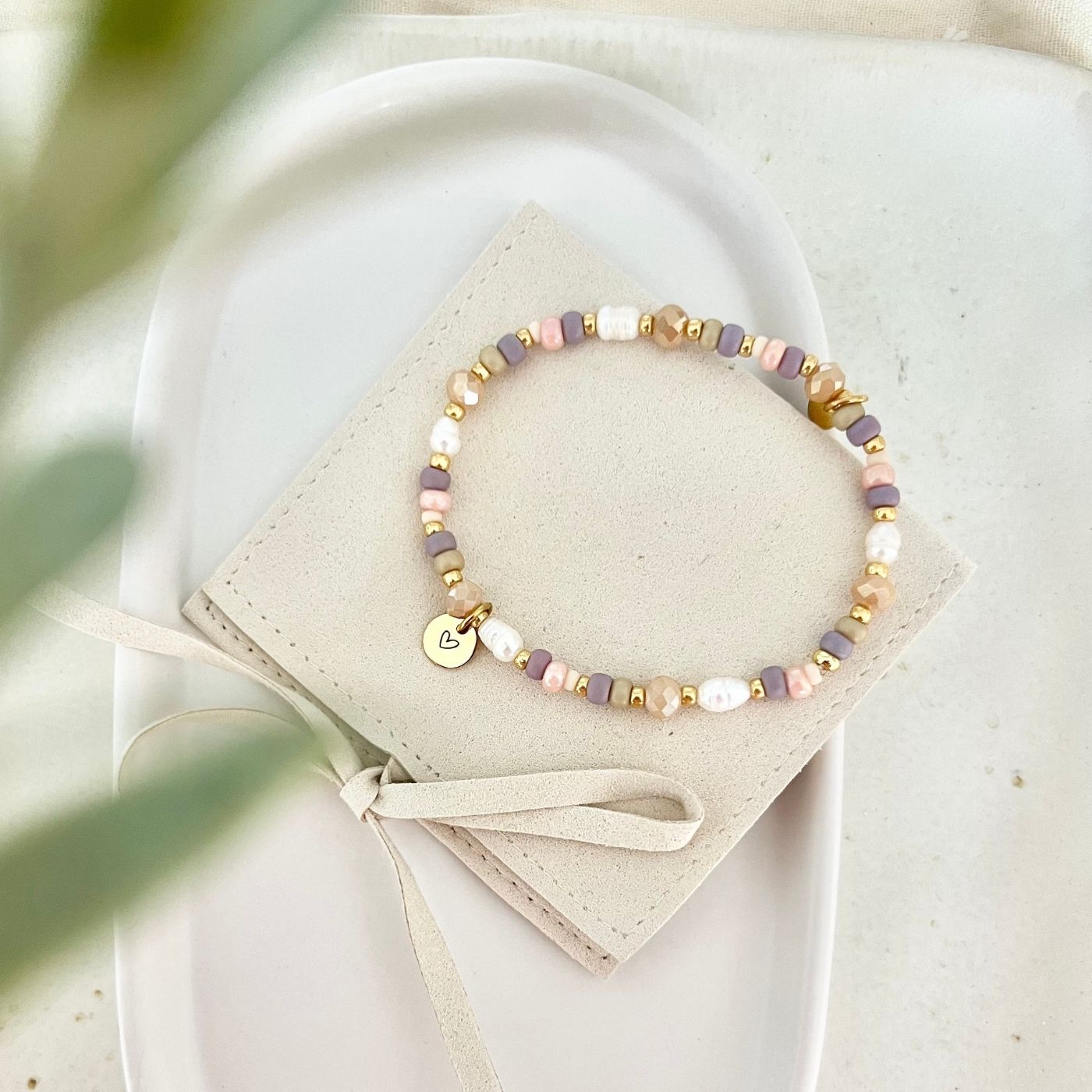 Gesamtansicht des Armbands auf einem beigefarbenen Schmuckbeutel mit Schleifenband, aufgenommen von oben auf heller Keramikschale.