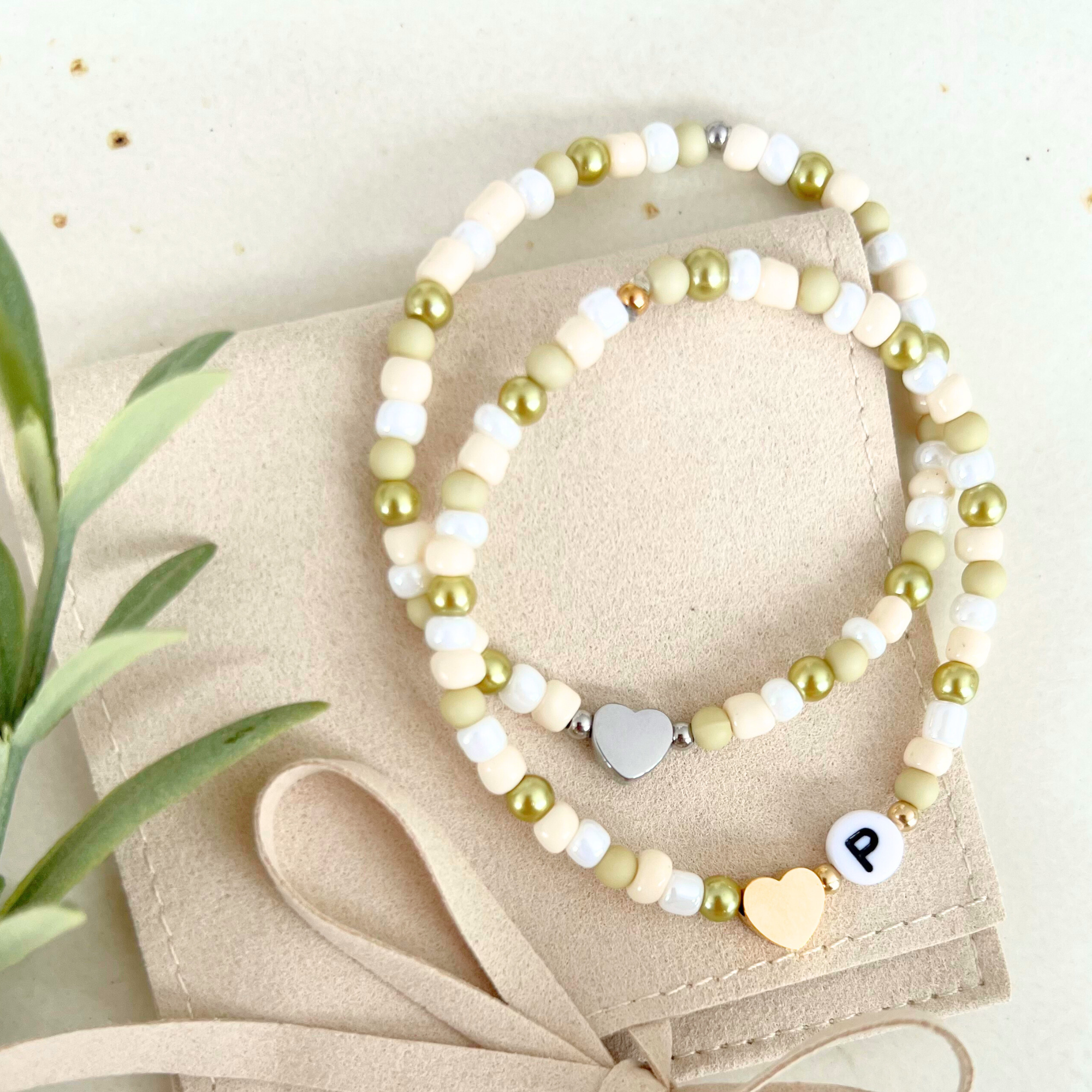 Gesamtansicht von zwei Armbändern aus dem DIY Kit VERDE – eines mit goldenem Herzanhänger und Buchstaben „P“ und das andere mit silbernem Anhänger. Perfekt für DIY Geschenke oder kreative Bastelstunden.