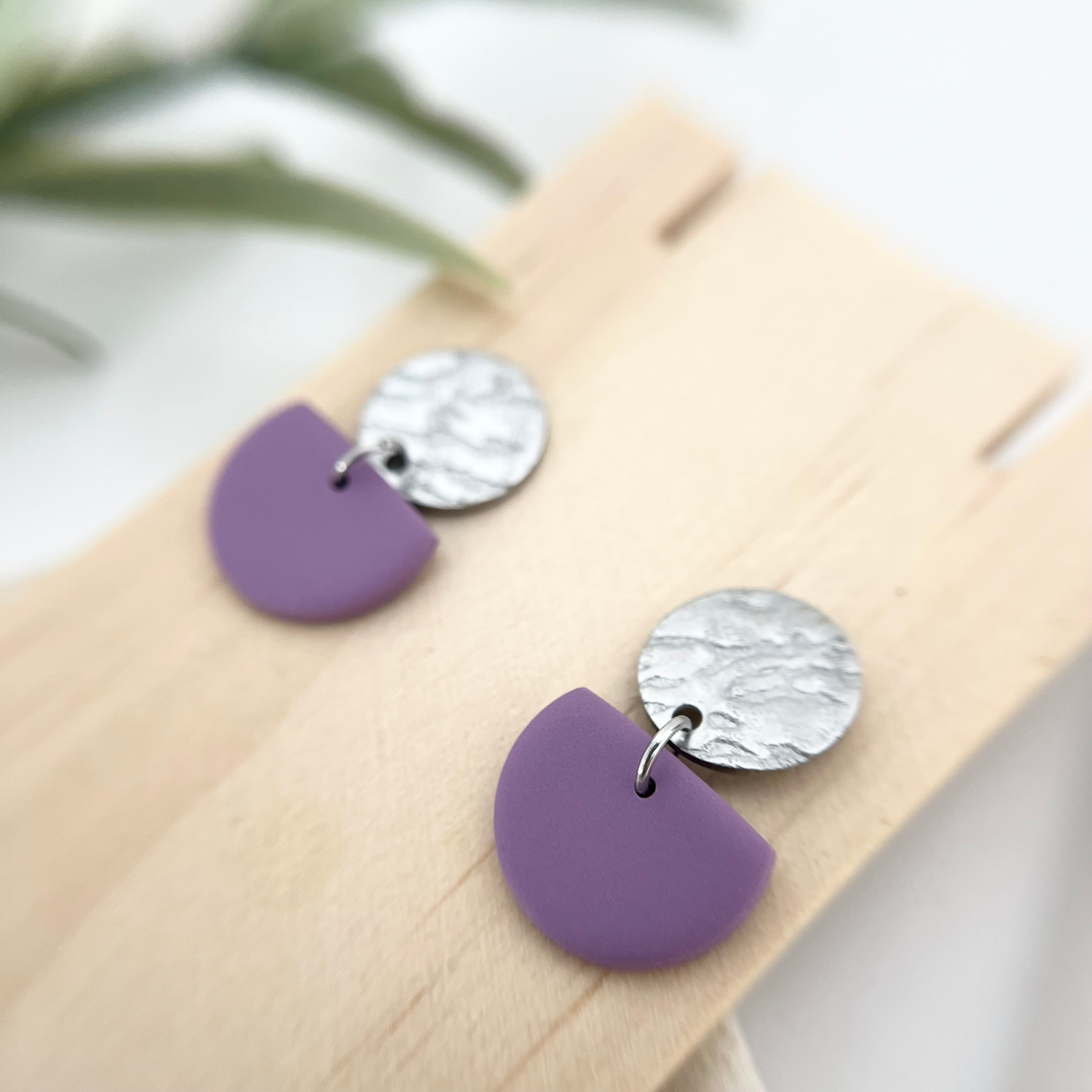 Zarte Ohrringe ALMERIA in Lila mit silberfarbenem Edelstahl, die minimalistisches Design und moderne Eleganz vereinen, abgebildet auf Holz