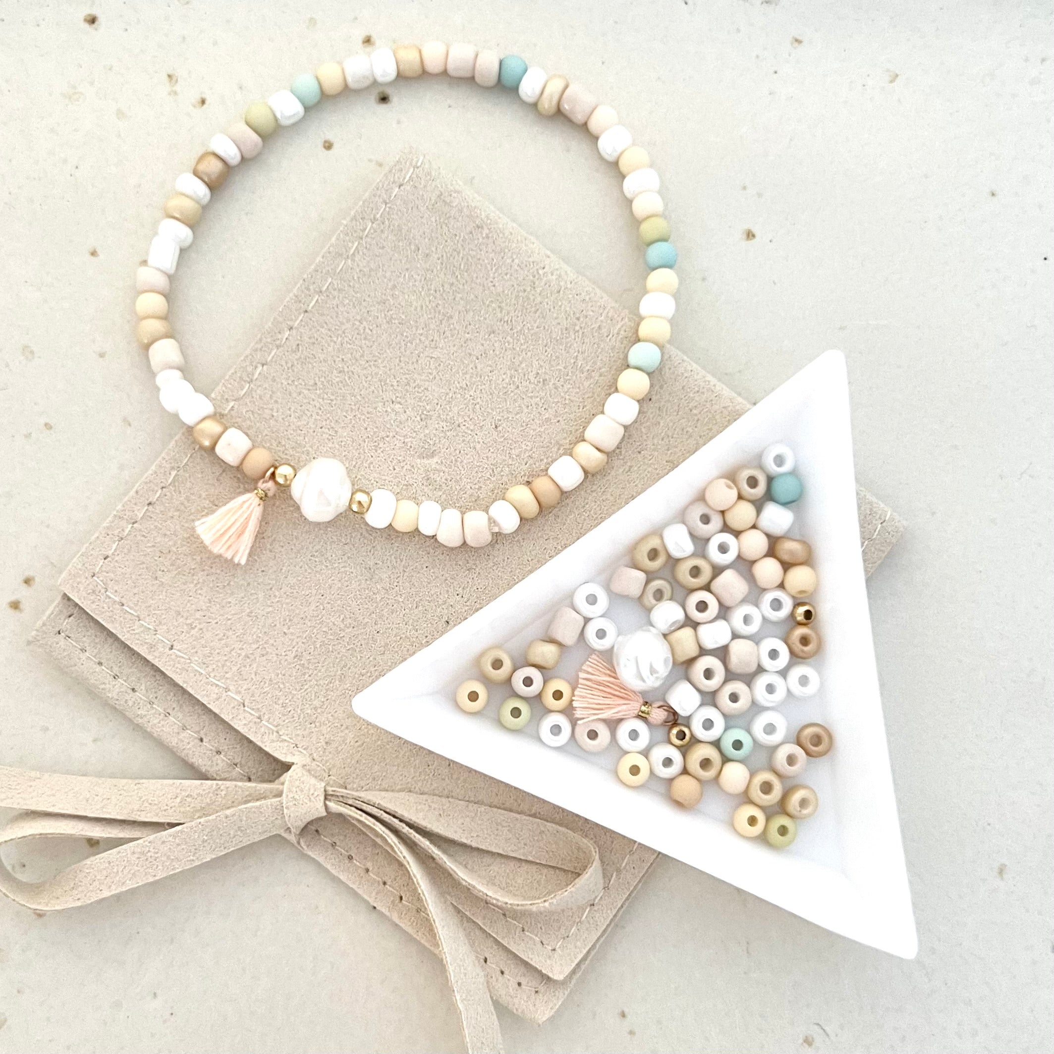 Foto von oben Armband und Perlen in weißer Schale auf einer cremefarbenen Tasche – Perlen und Armbänder im DIY Workshop für kreative Schmuckgestaltung