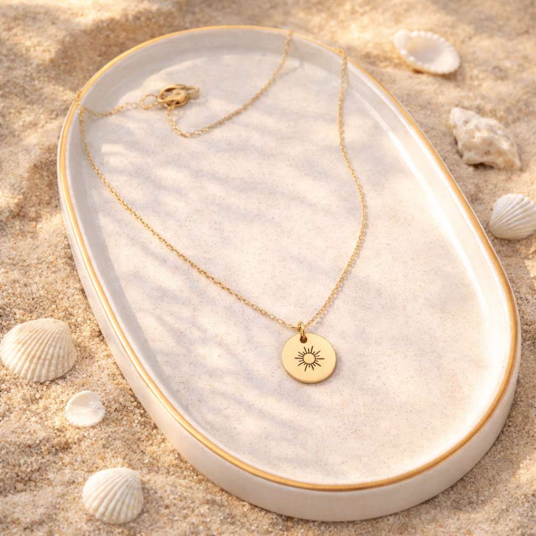 Goldfarbene Kette mit rundem Sonnen-Anhänger liegt auf hellem Tablett im Sand mit Muscheln, geeignet als Schmuck für Urlaub, Strandlooks oder als Geschenkidee