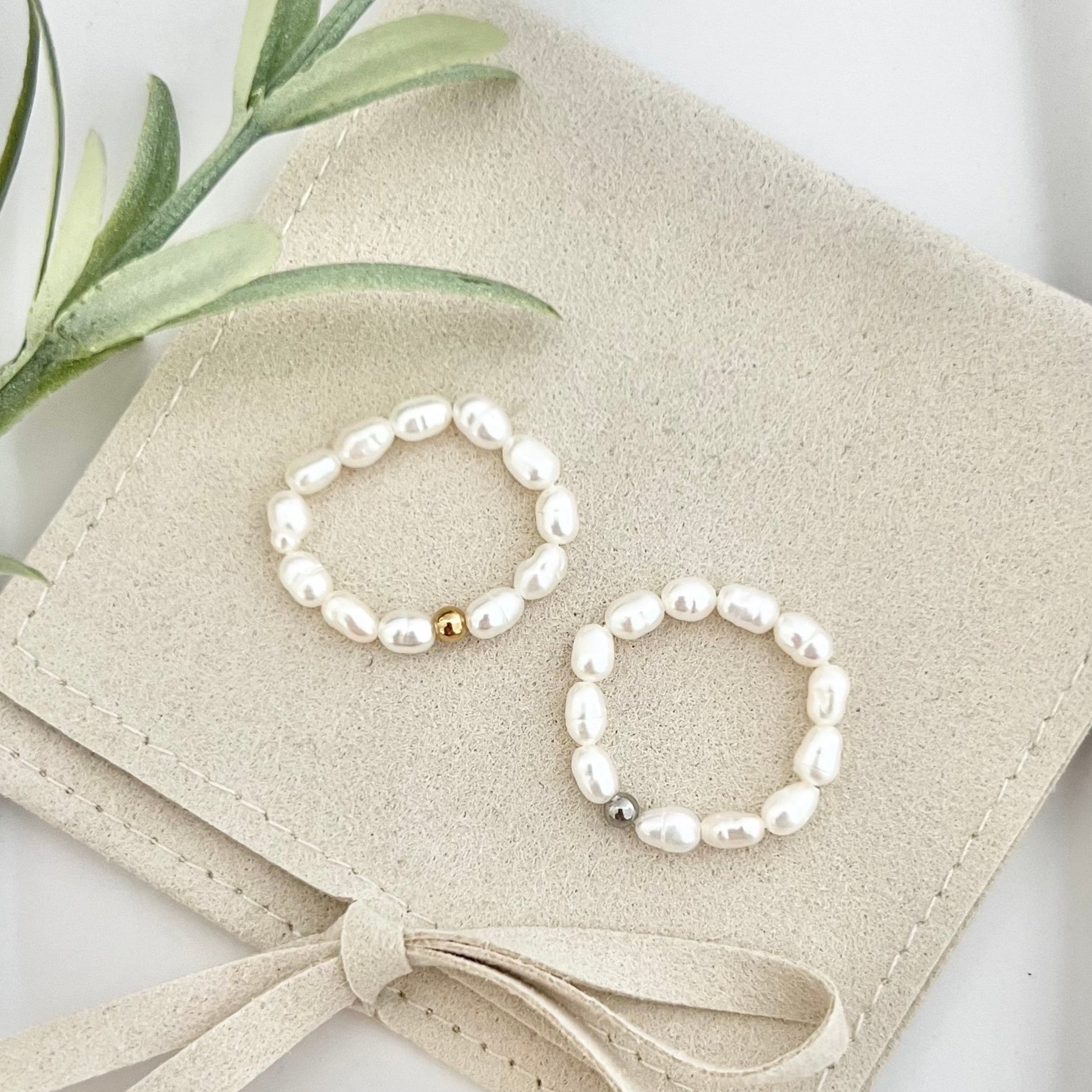 Zwei unauffällige Ringe aus kleinen weißen Süßwasserperlen auf elastischem Gummiband, präsentiert auf einer beigen Schmucktasche, eleganter und minimalistischer Schmuck der gerne für Freundinnen oder die Schwester verschenkt wird.