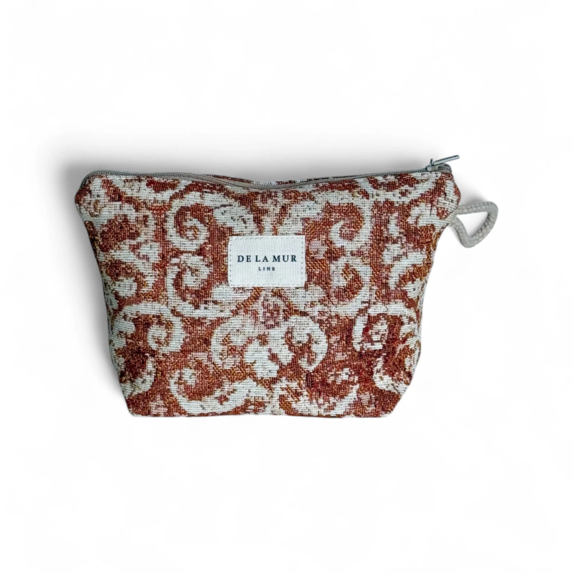 Eine rechteckige Kosmetiktasche mit rostbraun-beigem Jacquardmustel vor weißem Hintergrund. Oben verläuft ein grauer Reißverschluss, seitlich hängt eine kleine Schlaufe. Mittig befindet sich ein weißes DE LA MUR Label, Barockes Design.