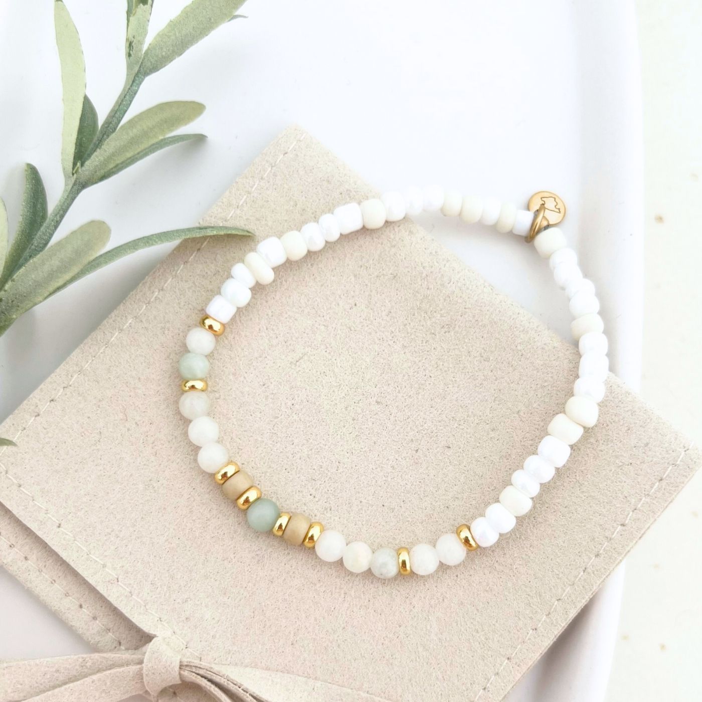 Vollansicht des Armbands BELLINI in einer eleganten Tasche, mit einem goldenen Gravur-Anhänger und Natursteinperlen als Glücksbringer