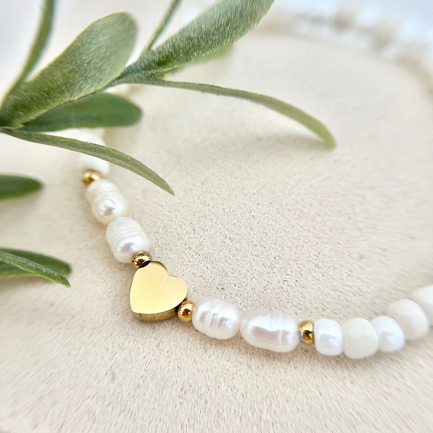 Nahaufnahme des goldfarbenen Herzanhängers auf dem Cremeweiß Süßwasserperlen-Armband