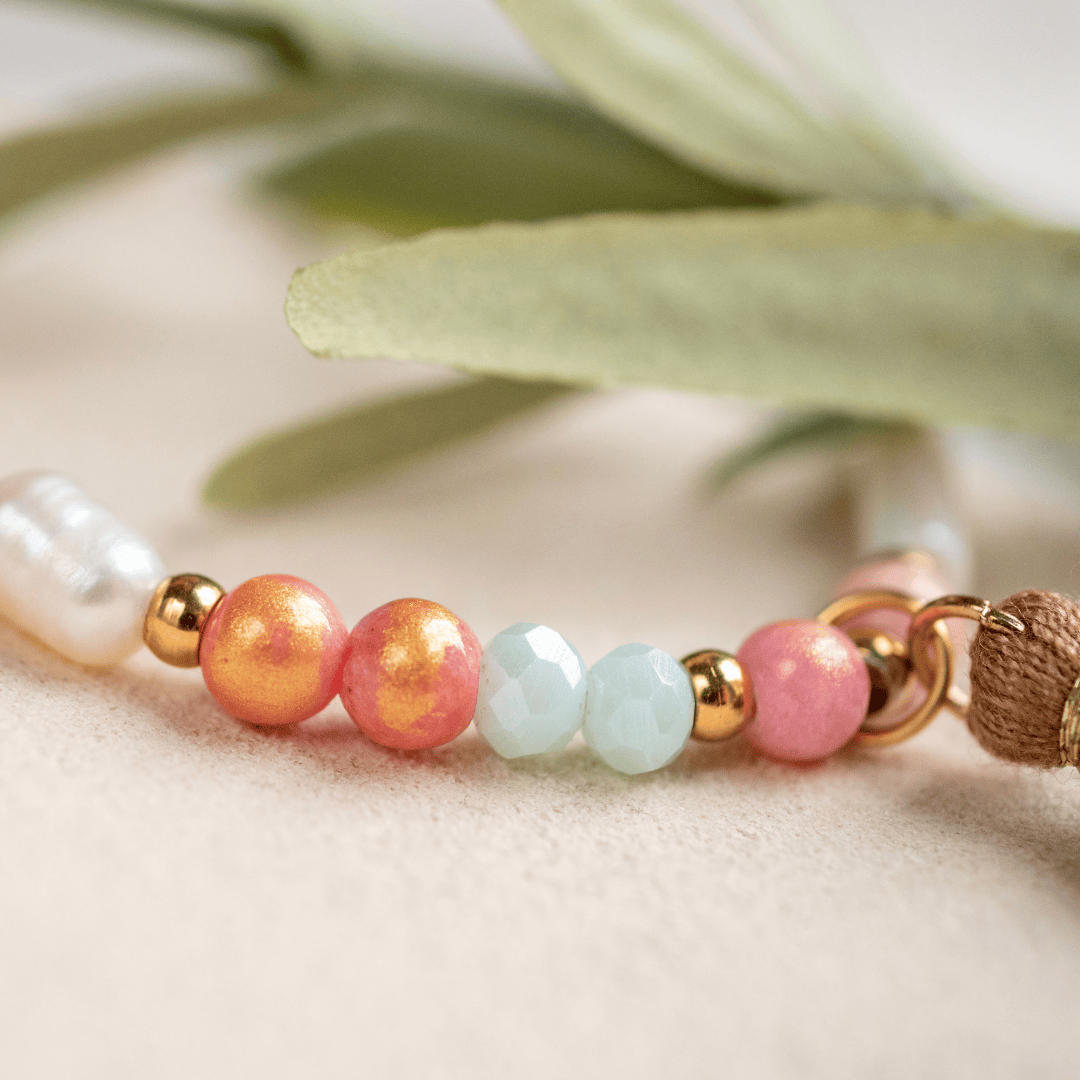 Detailaufnahme der Natursteinperlen des Armbands PORTO, in Mint- und Apricot-Tönen, mit einer Pflanze unscharf im Hintergrund