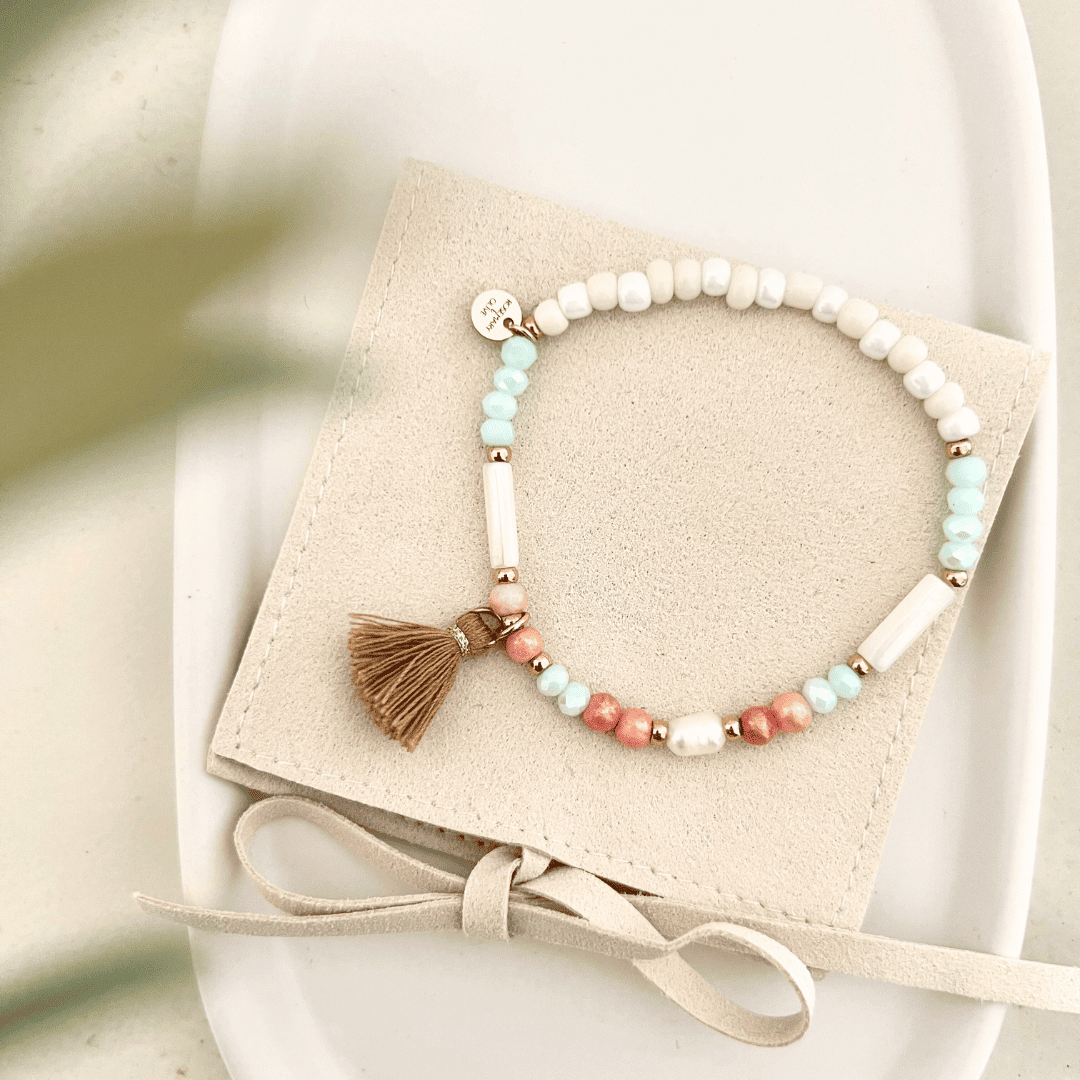 Vollansicht des Armbands PORTO auf einem Tablet, das den Stoffanhänger, Gravuranhänger und Muschelperlen in einer eleganten Tasche zeigt