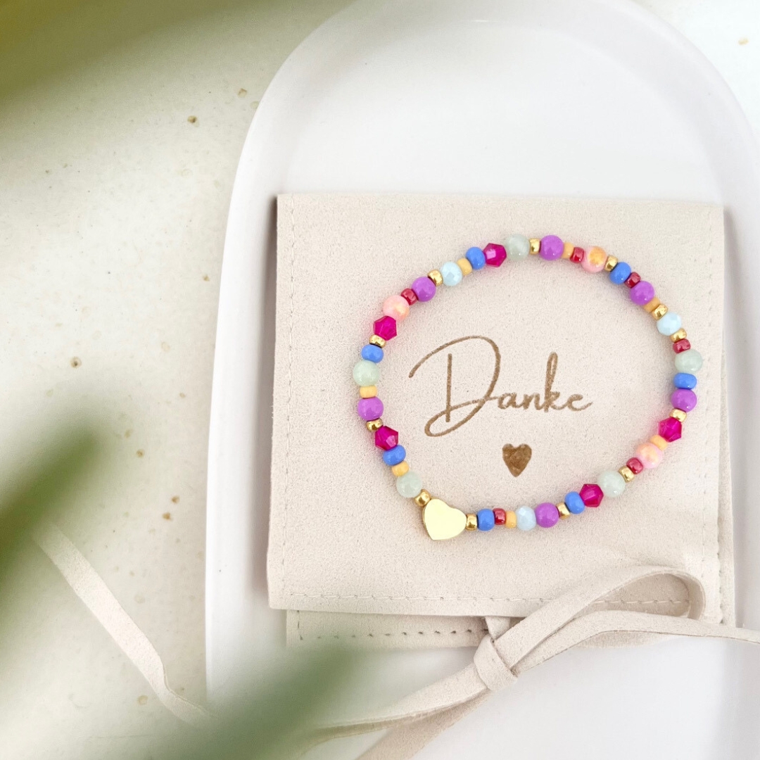 Buntes Armband aus Glas- und Natursteinperlen mit goldenem Herzanhänger, dekorativ präsentiert auf Schmuckbeutel mit Aufschrift ‚Danke‘ – Geschenkidee zum Danke sagen