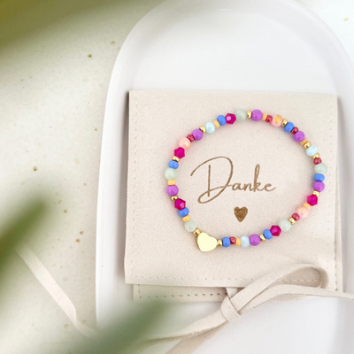 Buntes Armband aus Glas- und Natursteinperlen mit goldenem Herzanhänger, dekorativ präsentiert auf Schmuckbeutel mit Aufschrift ‚Danke‘ – Geschenkidee zum Danke sagen
