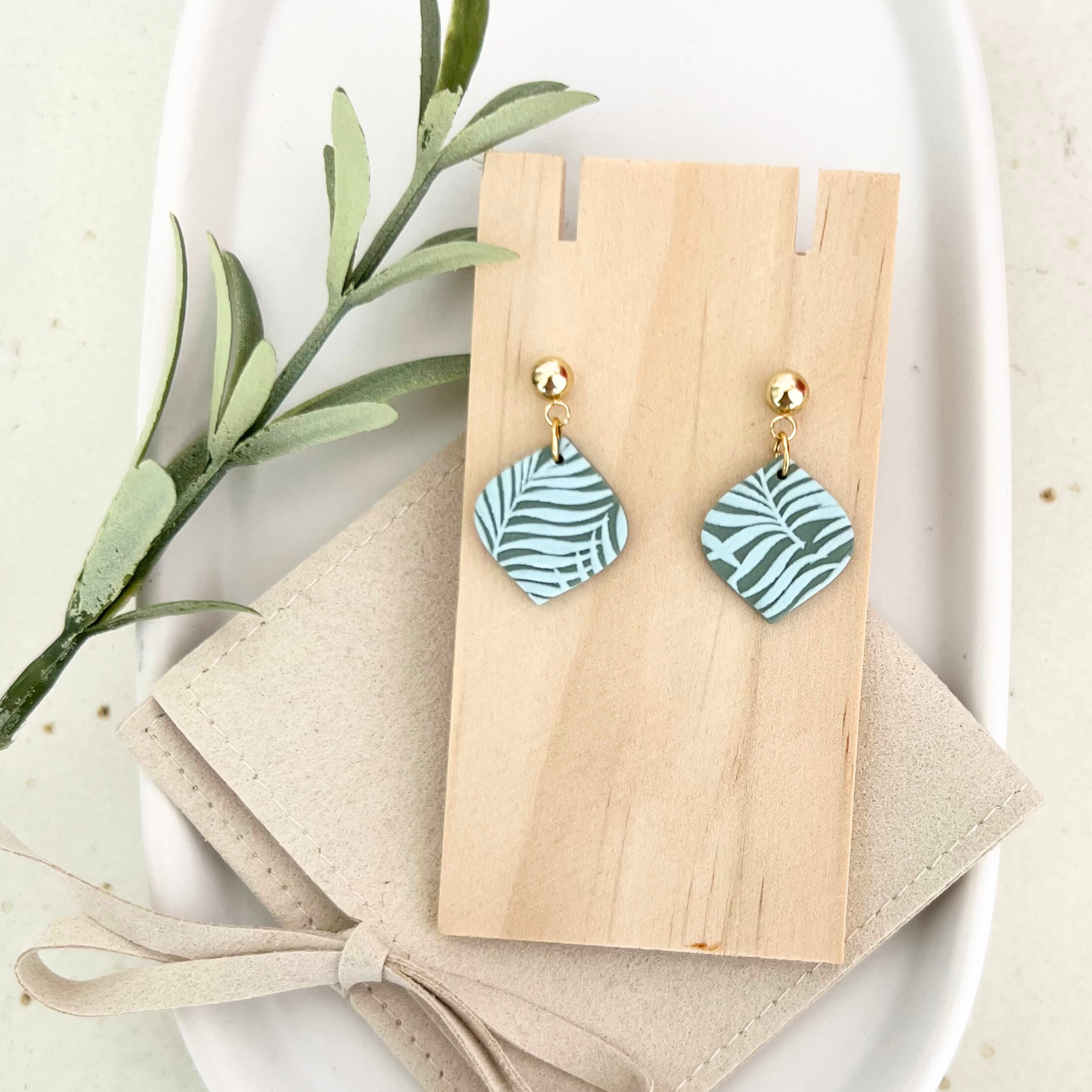 Detailaufnahme der Ohrringe HOJA mit Palmenblatt-Design aus Polymer Clay und Edelstahl-Stecker, auf Holz mit Tasche fotografiert