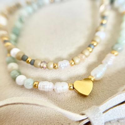 Nahaufnahme der goldenen Herzperle zwischen weißen Süßwasser- und grünen Steinperlen – ein zartes Symbol der Liebe und Freundschaft.