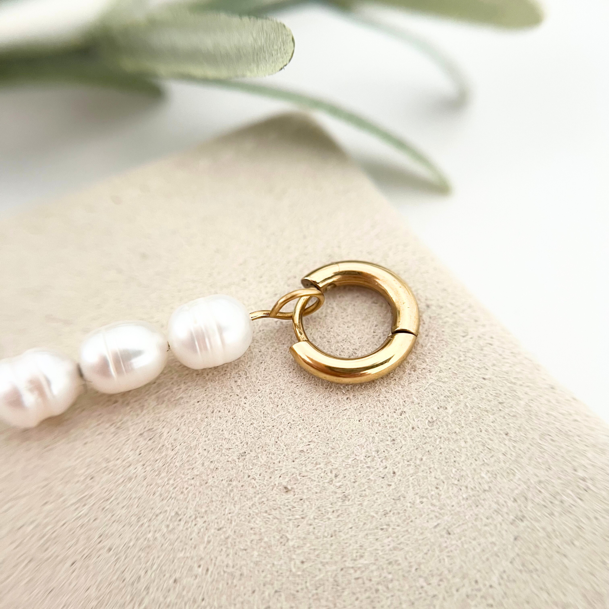 Nahaufnahme eines goldenen Edelstahl-Ohrrings PERLA mit schimmernder weißer Süßwasserperle, das die hochwertige Verarbeitung und Eleganz zeigt.